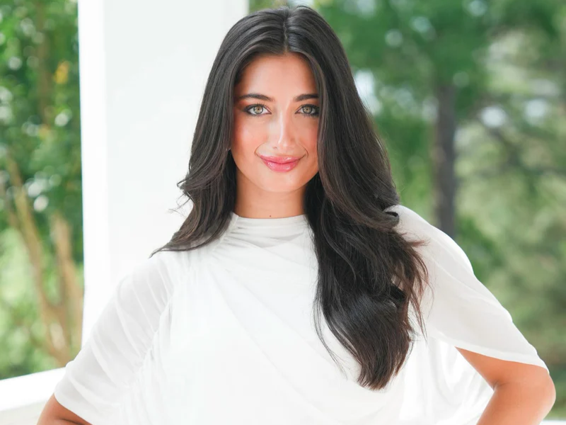 A woman with dark hair and wearing white smiles into the camera