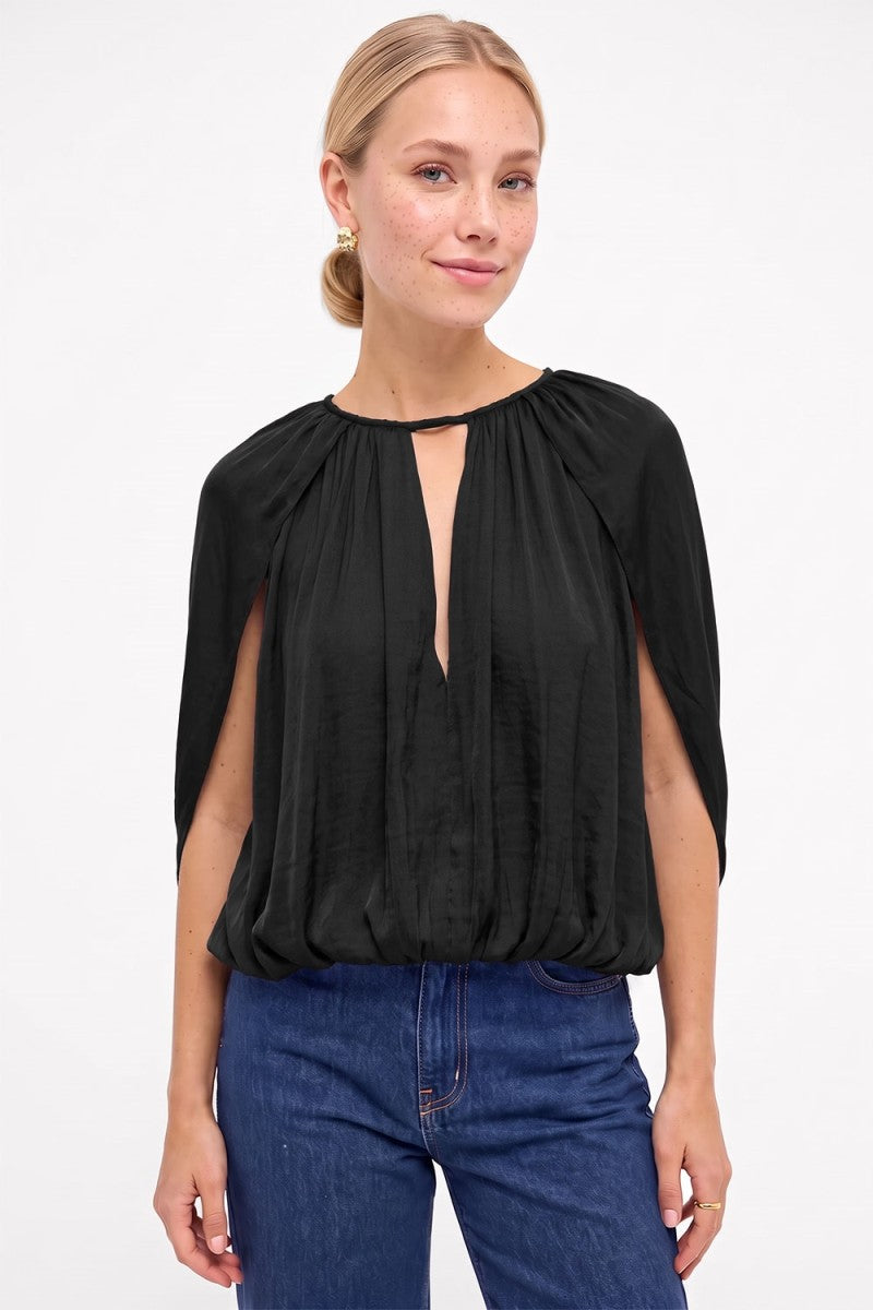 A woman wearing a black short-sleeve blouse with a keyhole cutout and blue jeans, photographed against a plain white studio background.