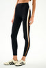 A model wearing black high-waisted leggings with a vertical cream and brown stripe down the side, paired with cream sneakers, against a plain white studio background.