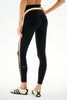 A model shown from the back wearing black athletic leggings with a white and beige side stripe, paired with white sneakers, on a white studio background.