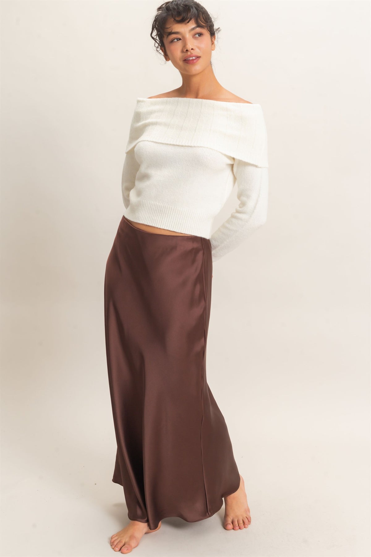 Woman wearing a white off-shoulder top and brown skirt on a plain background
