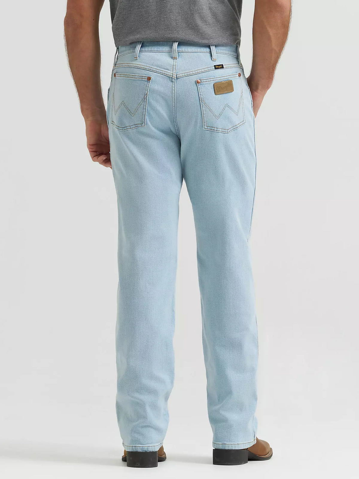 A person shown from the back wearing light-wash blue jeans, a gray shirt, and brown shoes against a plain light gray studio background.