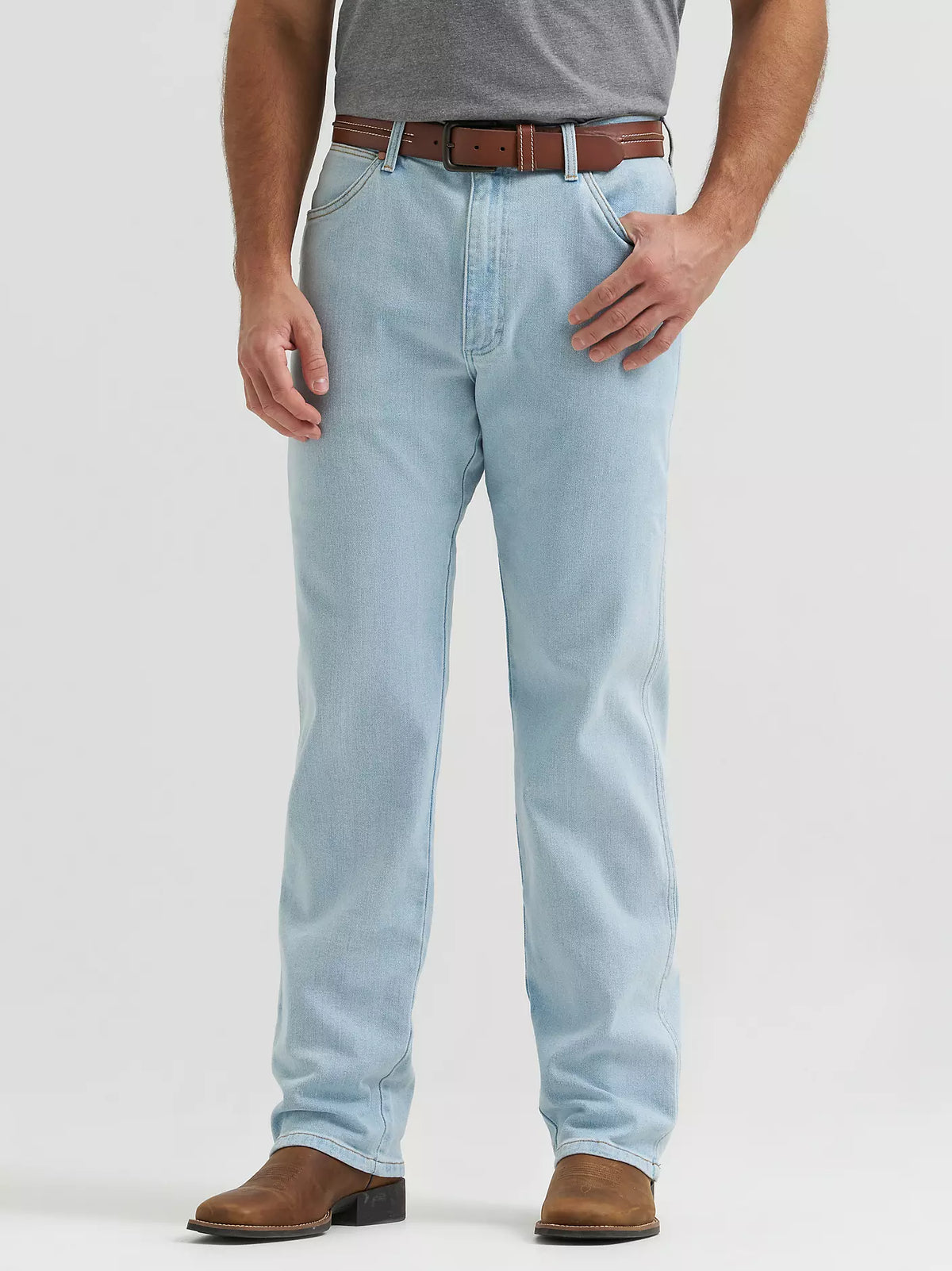 A person wearing light-wash blue jeans with a brown belt and brown boots, shown from the waist down against a plain light gray studio background.