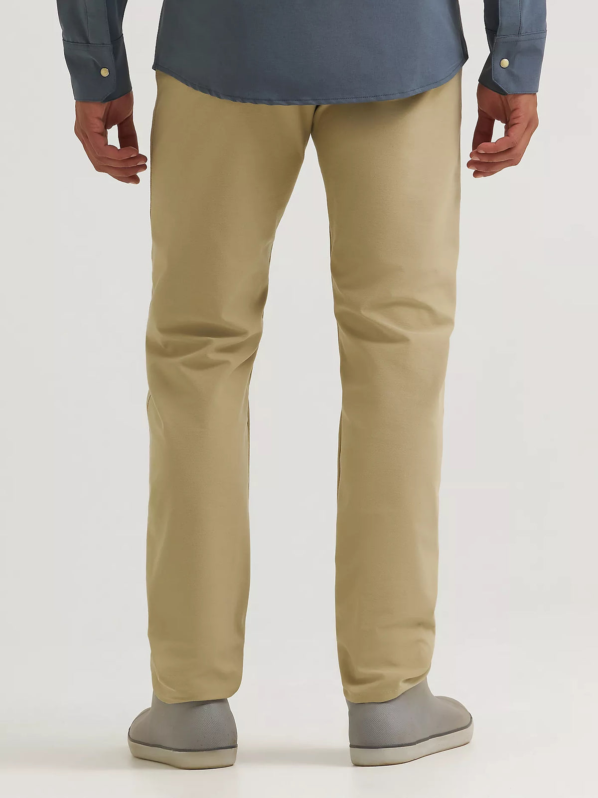 A person shown from the back wearing straight-leg khaki trousers, a blue shirt, and gray slip-on shoes against a plain light gray studio background.
