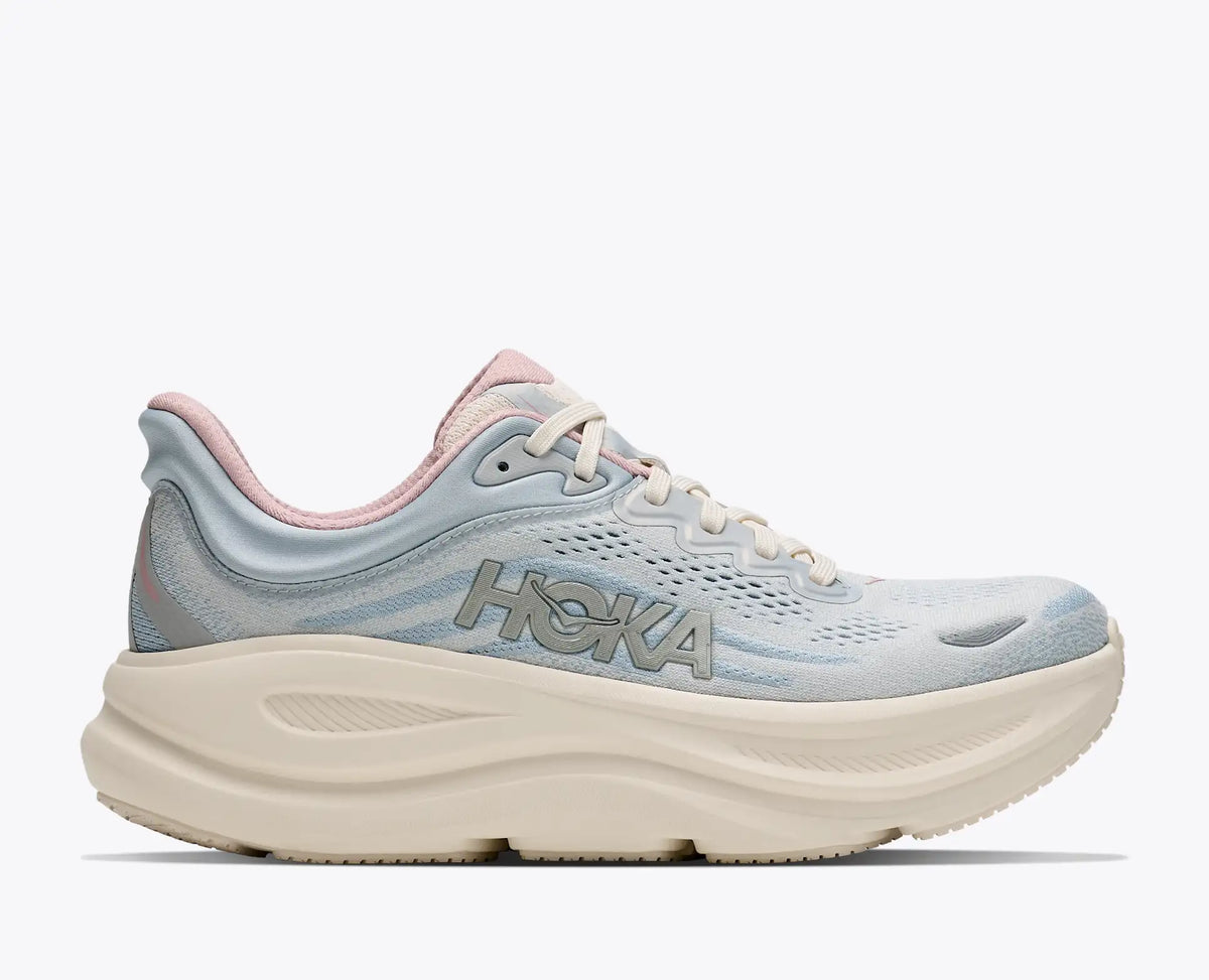 A HOKA running shoe in light blue and cream with a pink collar, shown from the side against a light gray background.
