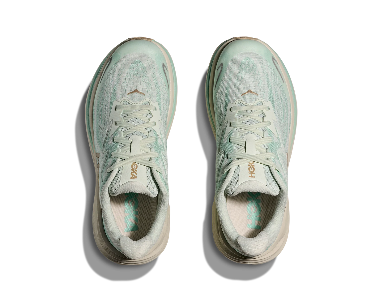 A pair of Hoka running shoes in a pale mint green and cream colorway, shown from a top-down view on a white background with soft drop shadows.