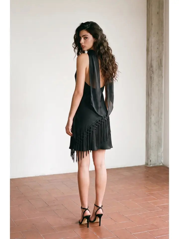 Woman standing in front of white wall wearing a black mini dress