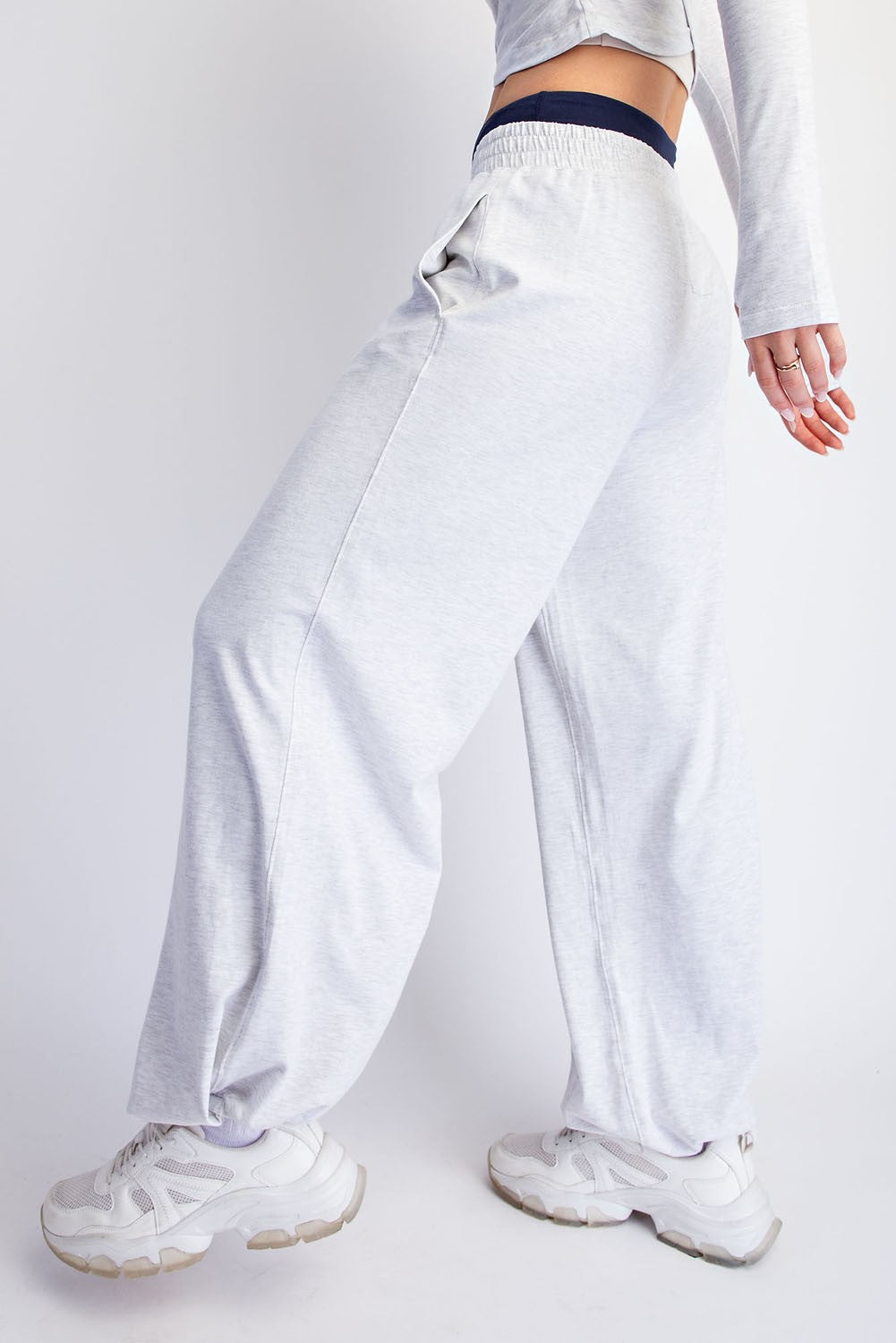A person wearing light heather gray wide-leg sweatpants with a dark elastic waistband, paired with white sneakers, shown from the waist down against a plain light gray studio background.