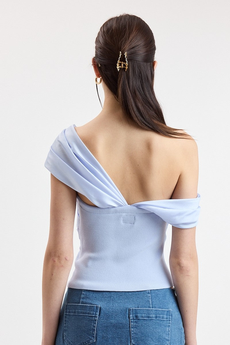 A woman shown from the back wearing a light blue off-the-shoulder top and blue jeans, with a gold hair clip holding her hair up against a plain light background.