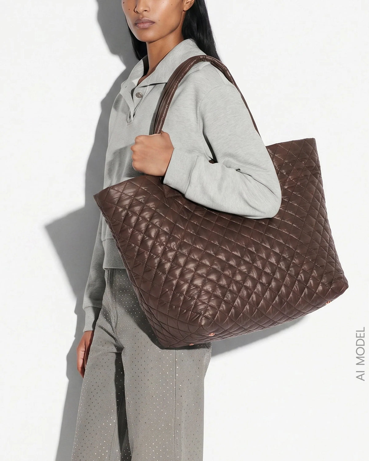 A model wearing a light gray sweatshirt and matching pants carries a large brown quilted leather tote bag against a white background with a strong shadow.