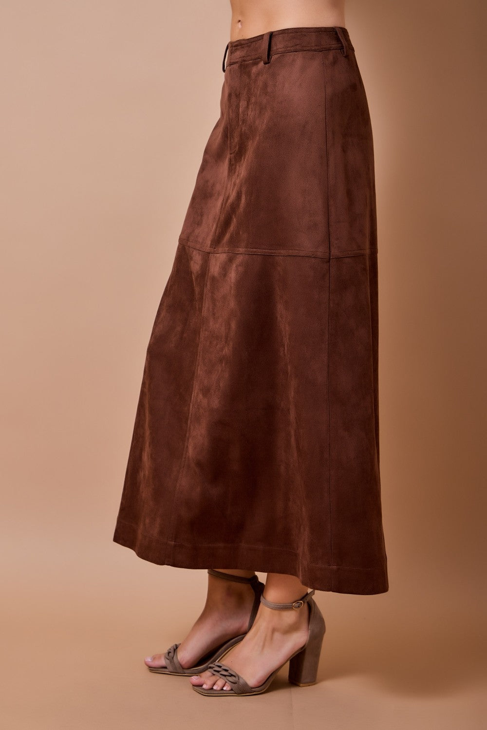 woman standing on tan background wearing brown suede skirt