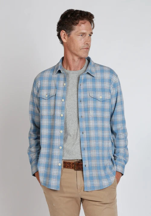Man standing wearing blue and white button down, khakis, and a belt in front of  a white background