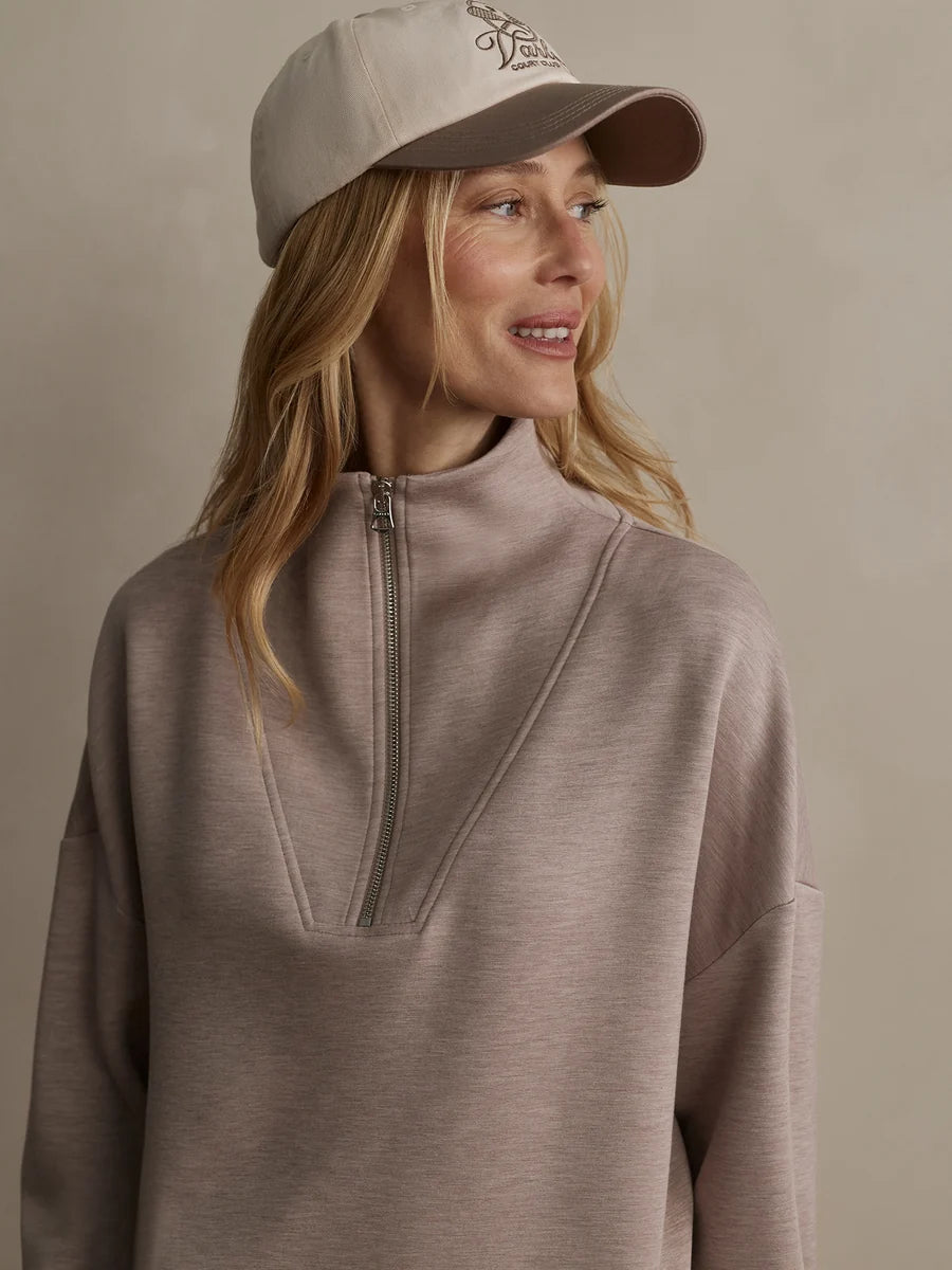 Woman wearing a beige cap and matching pullover against a neutral background