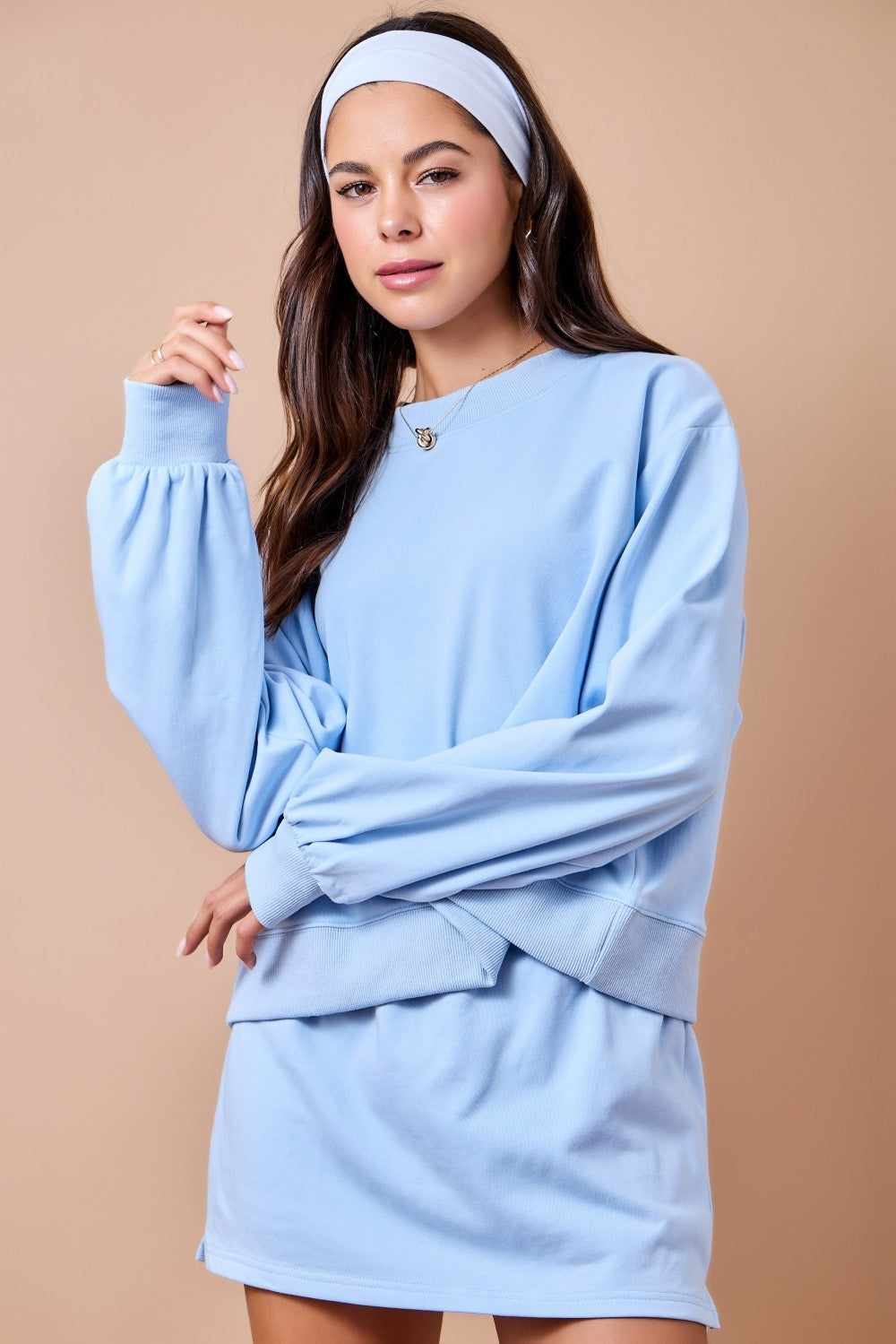 A woman modeling a light blue oversized long-sleeve sweatshirt dress with a matching headband, set against a solid beige studio background.