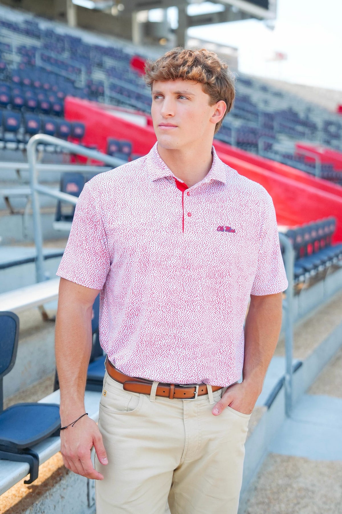 Man wearing a patterned pink shirt with a logo in an indoor sports facility.