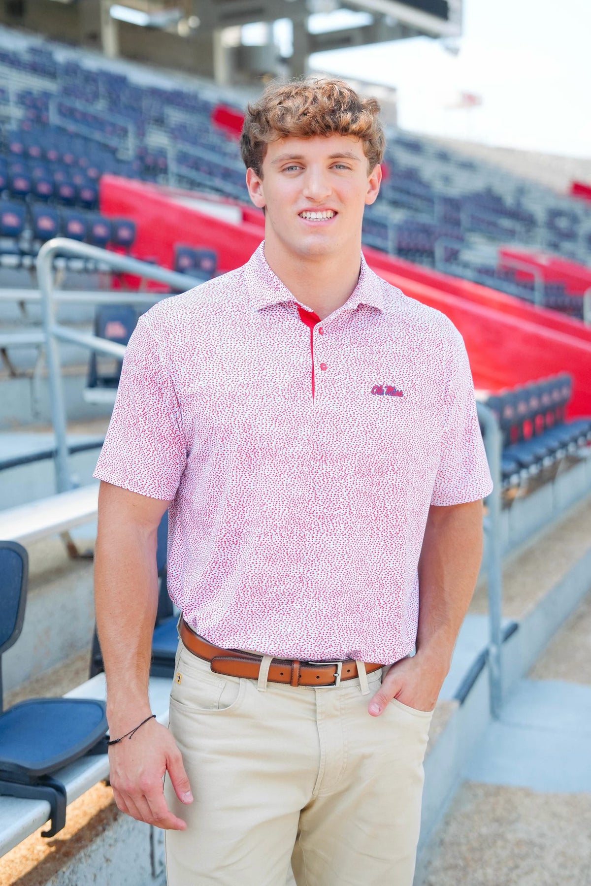 Man wearing a pink patterned polo shirt with a logo in an indoor sports facility.
