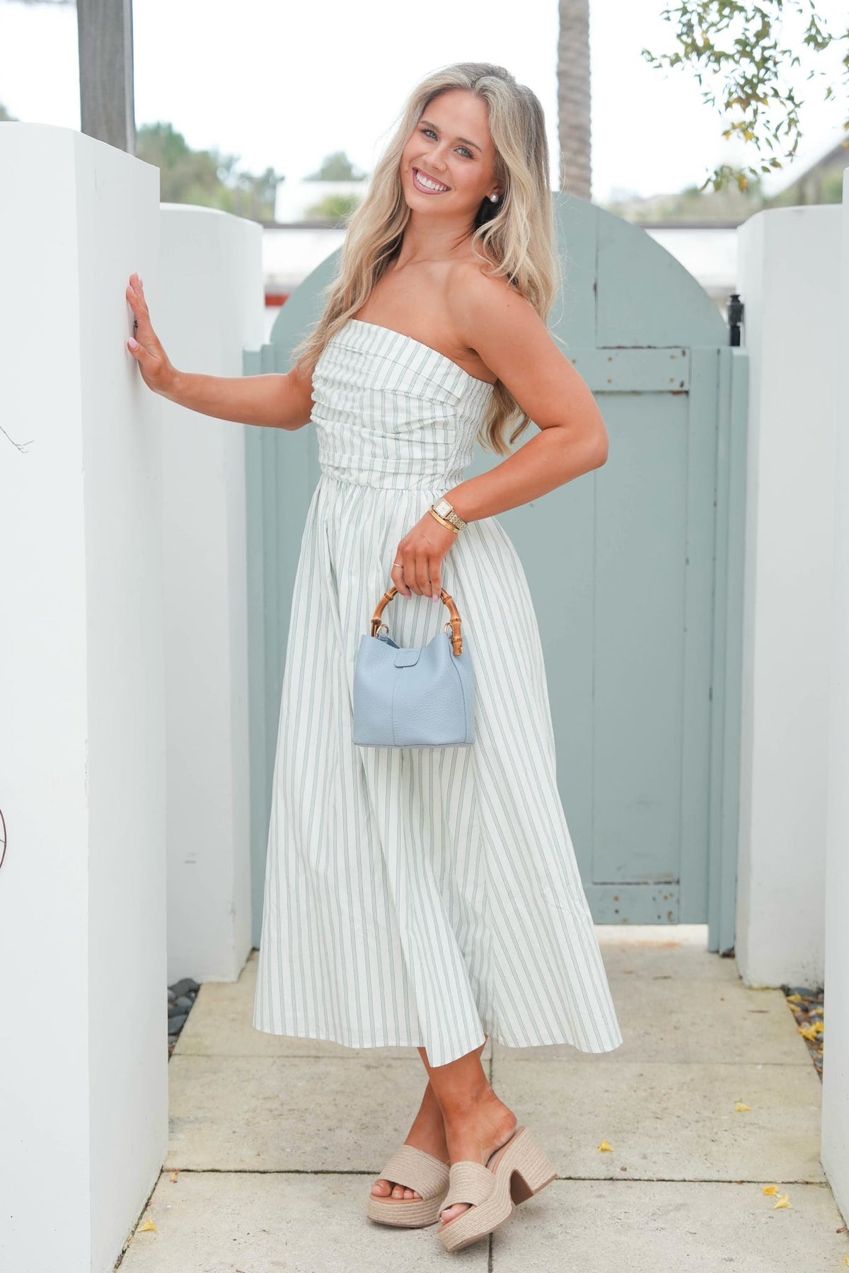 Woman in a white strapless dress holding a blue handbag outdoors.