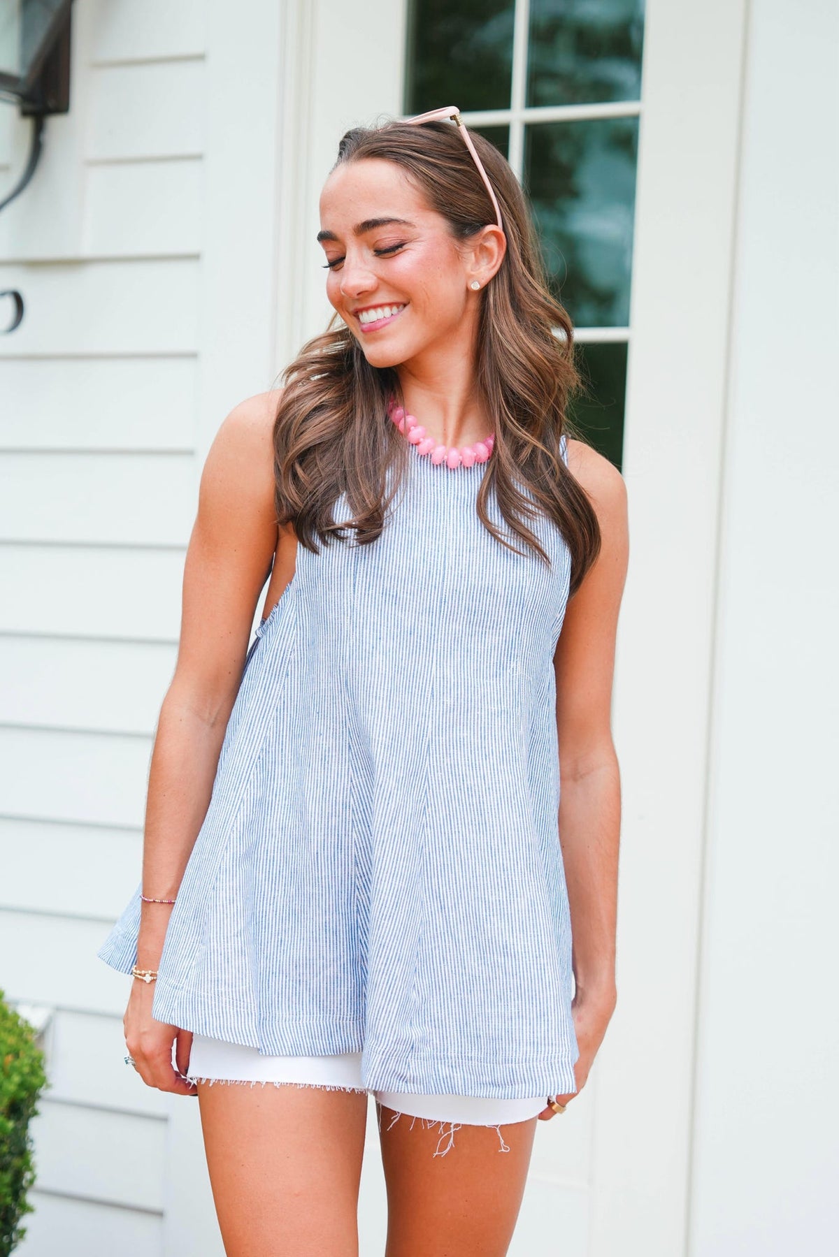 Woman wearing a light blue sleeveless dress with white shorts, standing outdoors.