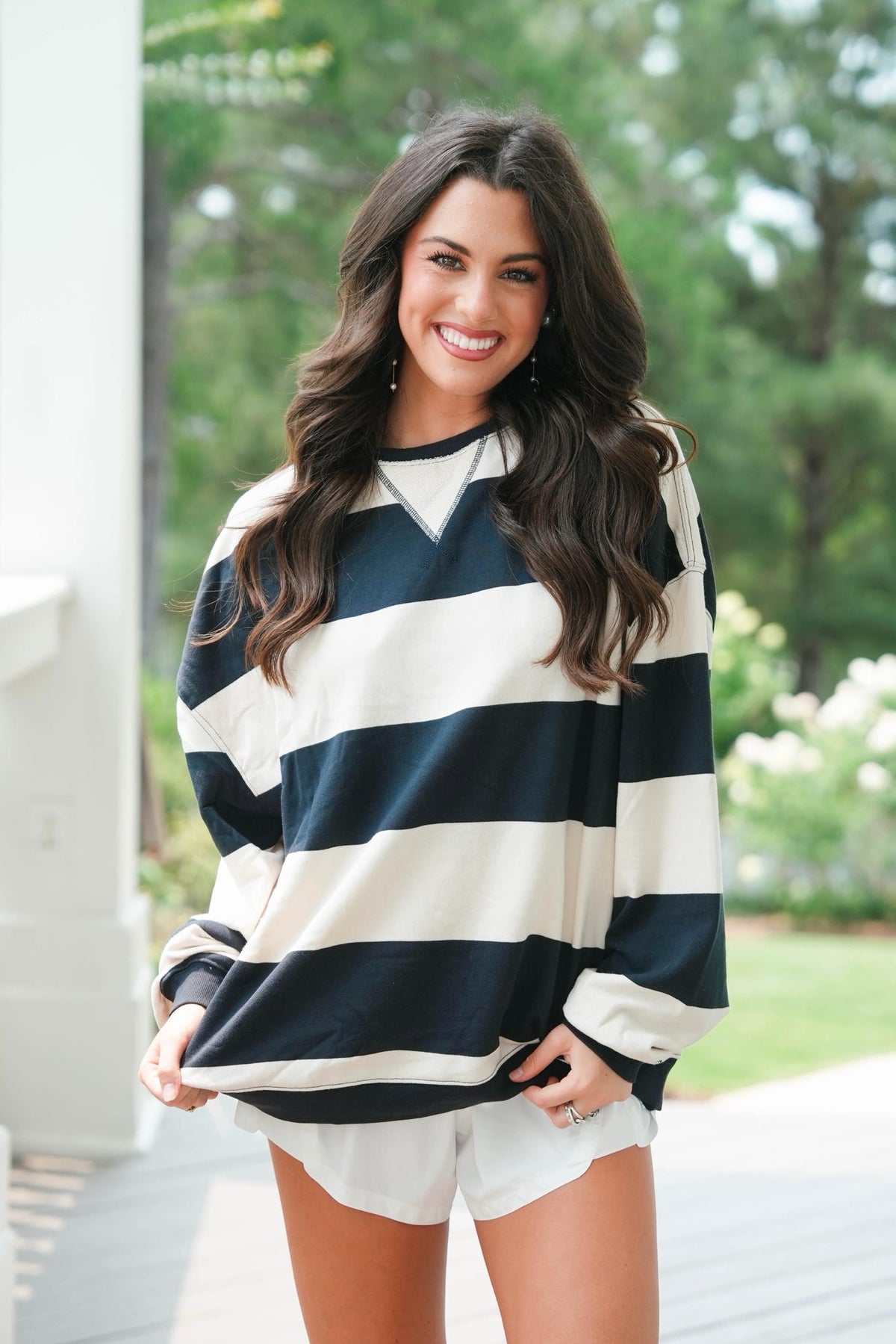 Woman wearing a navy and white striped sweater with white shorts outdoors.