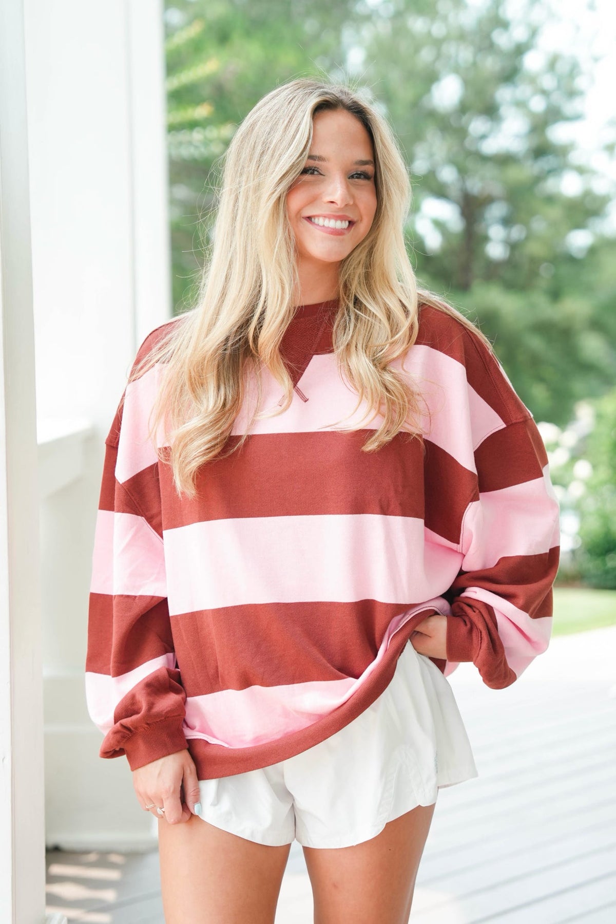 Woman wearing a red and pink striped sweater with white shorts outdoors.