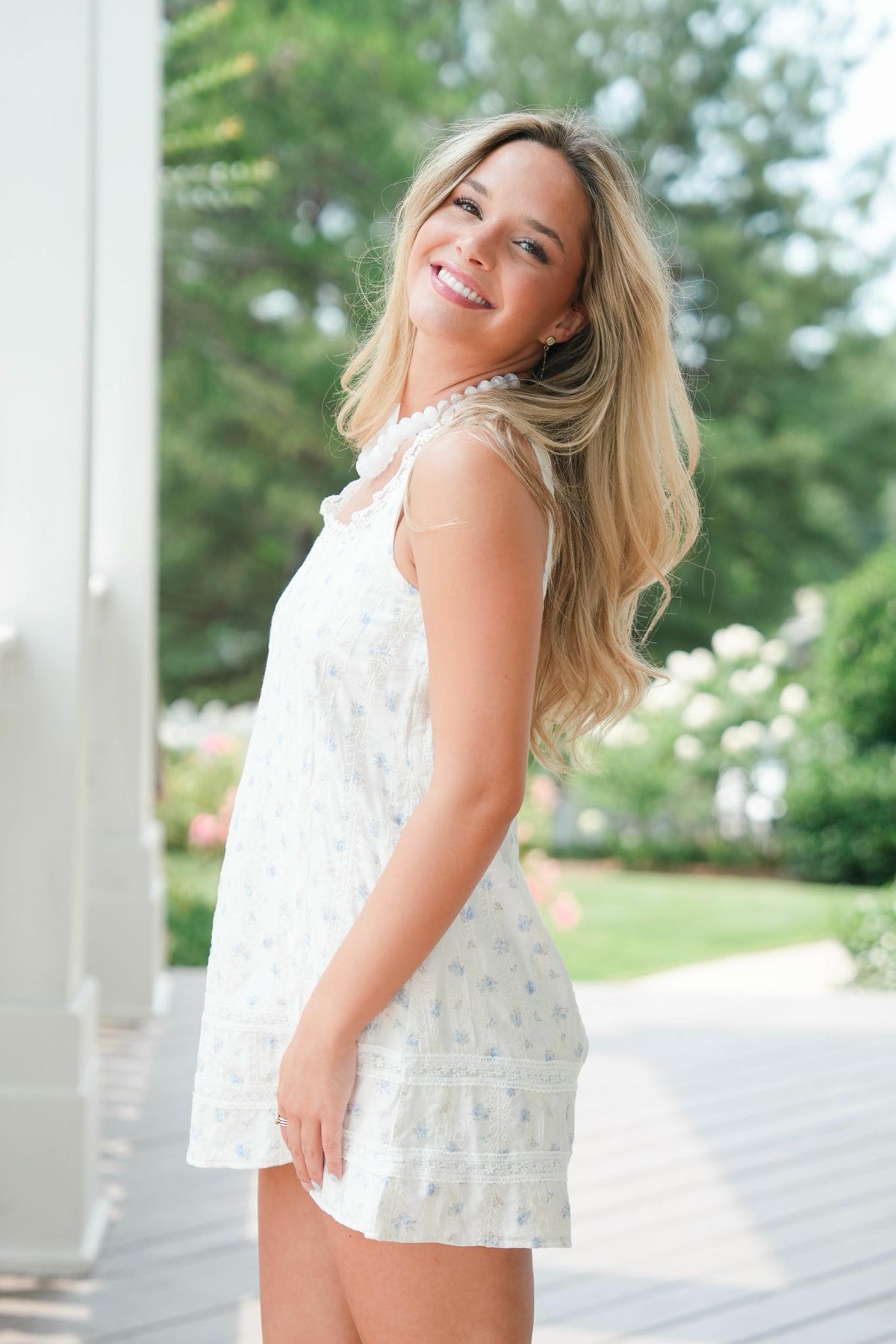 Woman in a white dress standing outdoors with greenery in the background