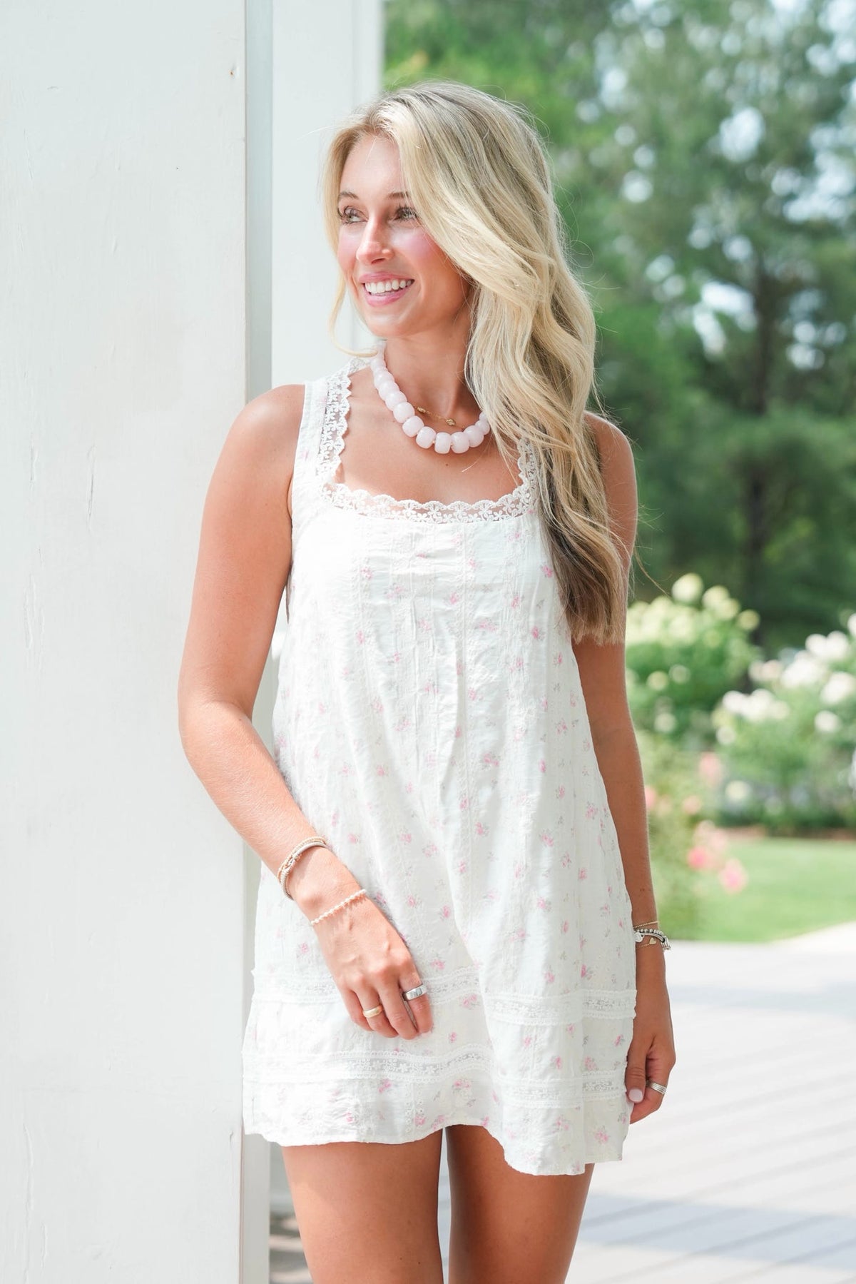 Woman wearing a white lace dress outdoors with greenery in the background