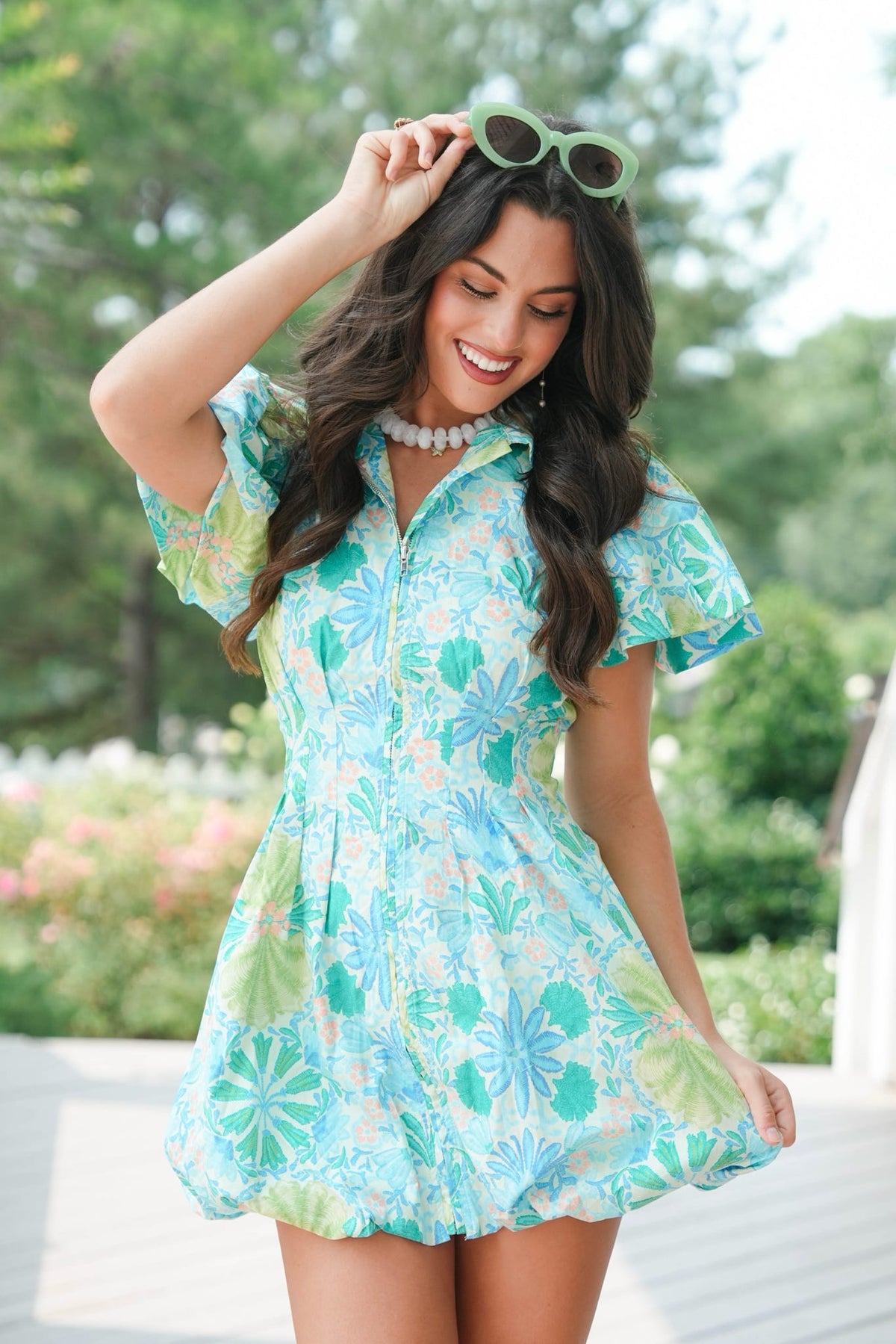 Woman wearing a floral dress with sunglasses on her head, standing outdoors.