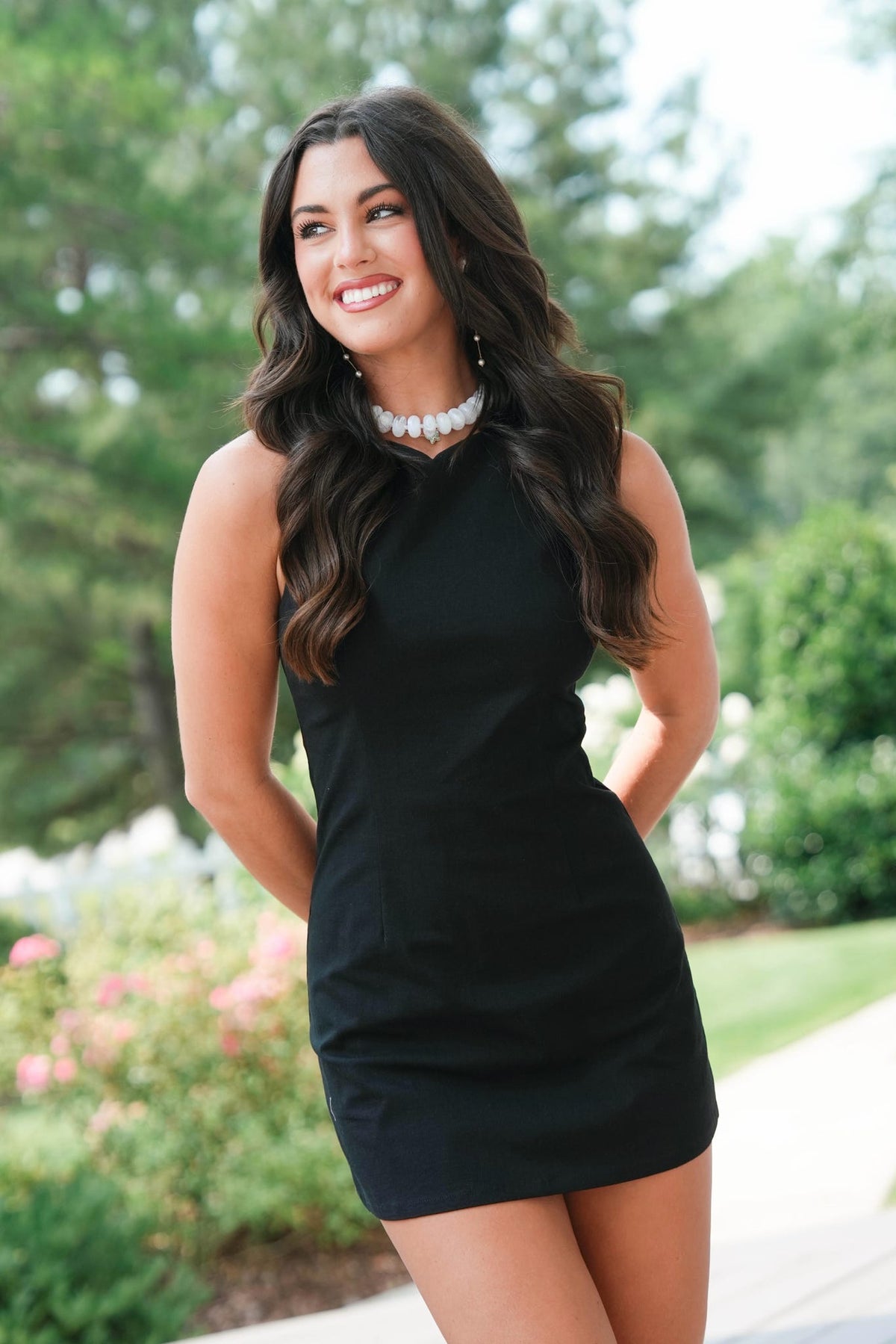 Woman in a black dress standing outdoors with greenery in the background