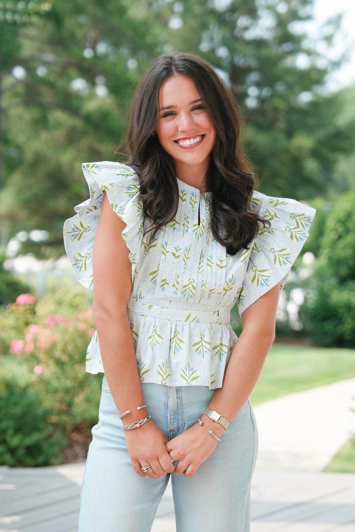 Woman wearing a light green floral blouse with ruffled sleeves outdoors.