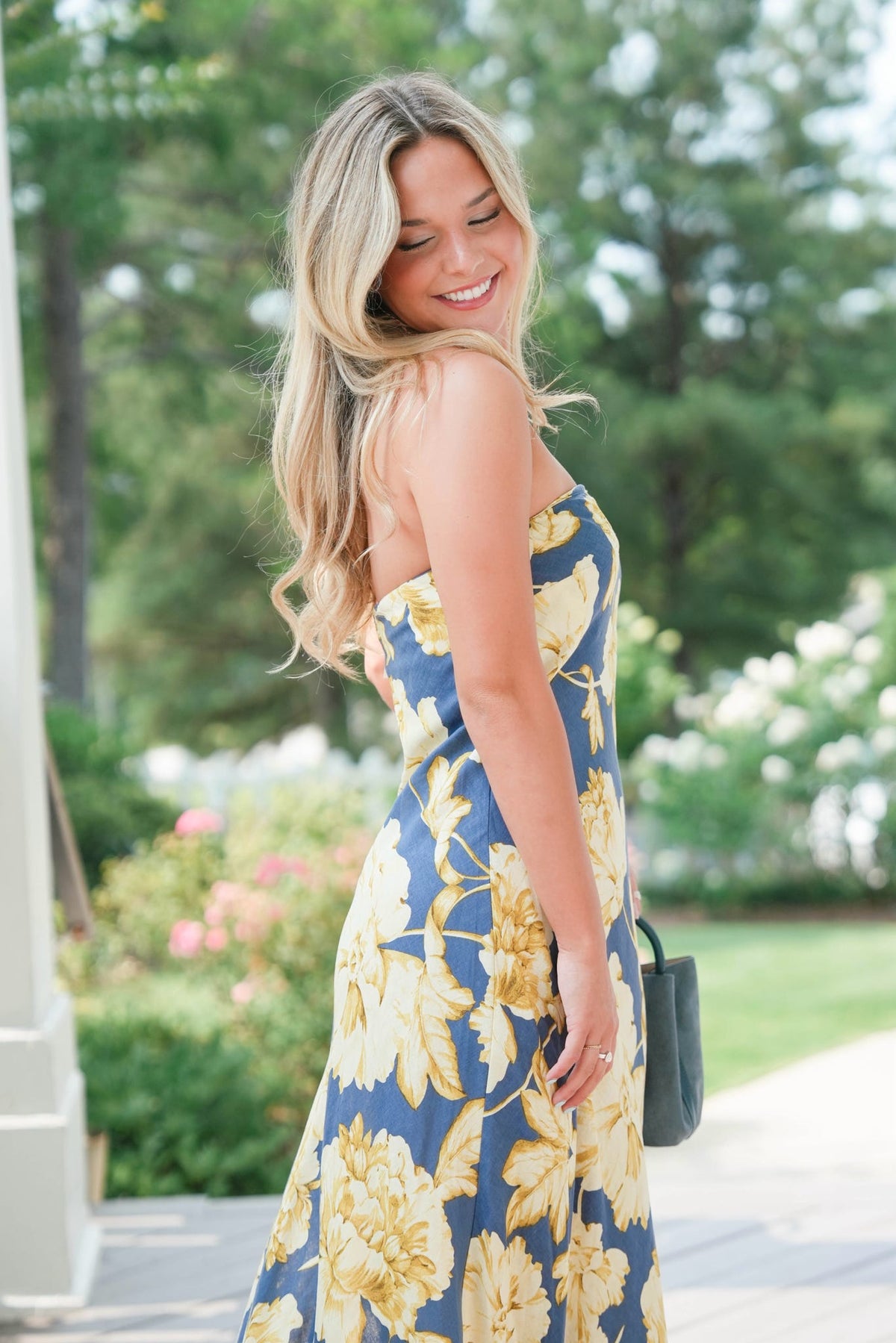 Woman in a blue floral dress standing outdoors with greenery in the background