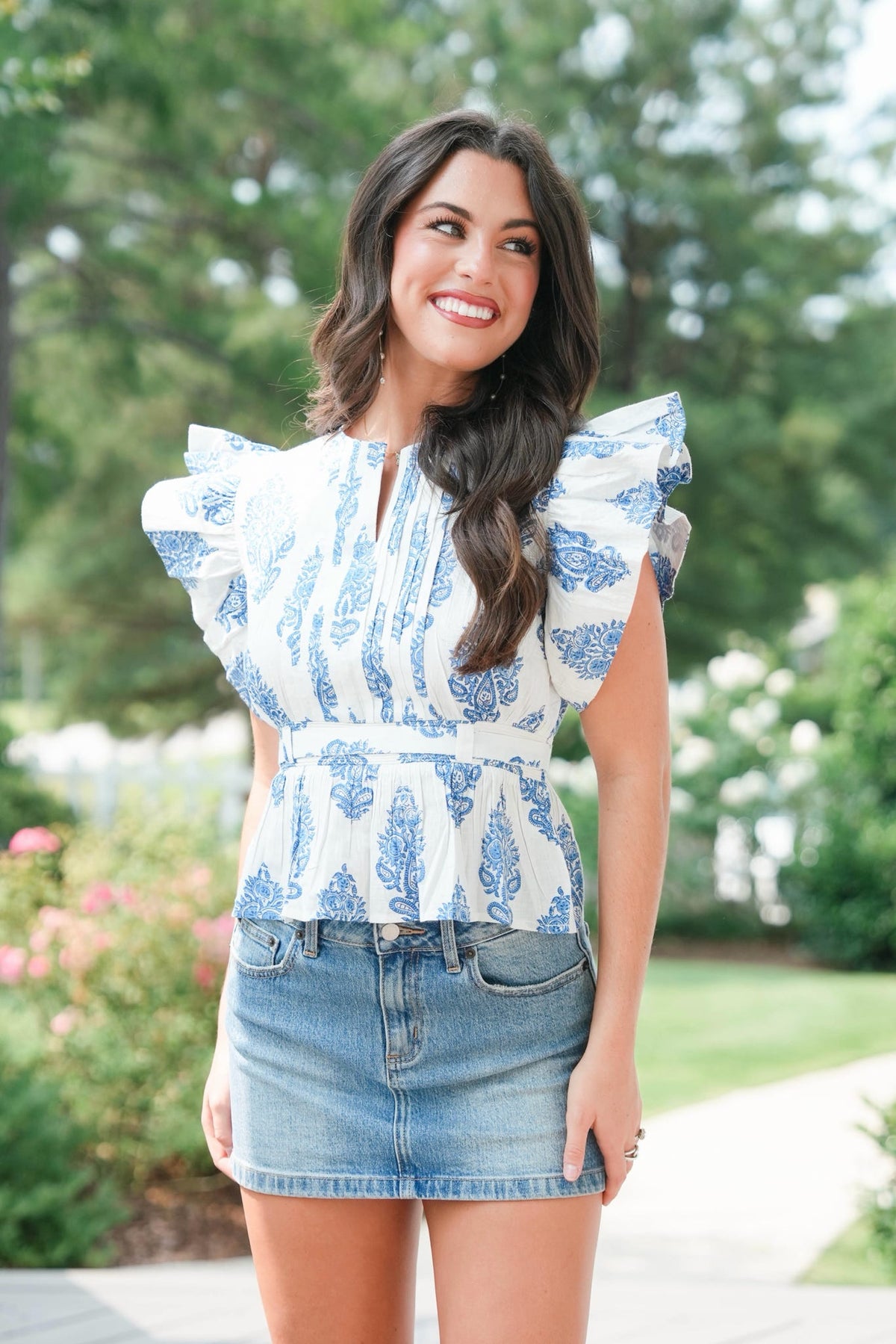 Woman wearing a blue and white patterned top with ruffled sleeves outdoors.