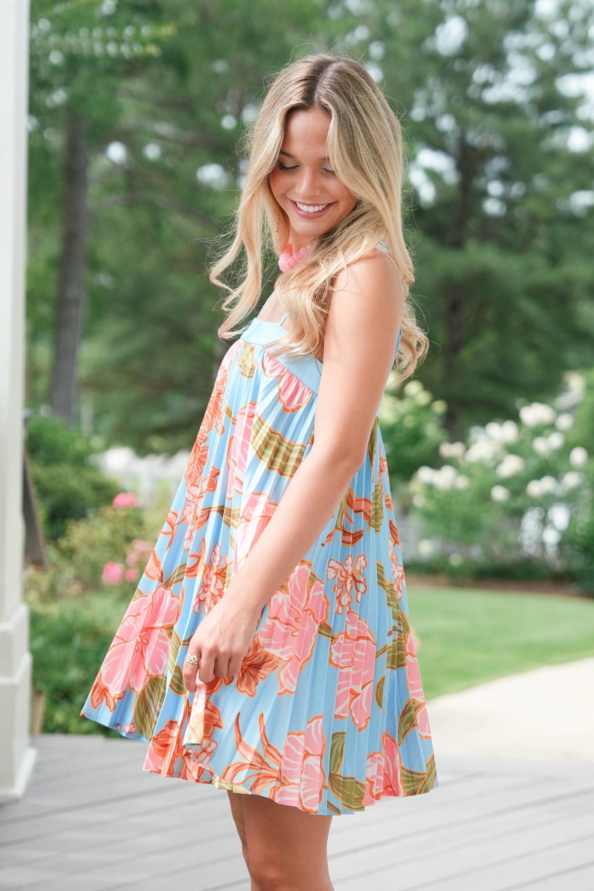 Woman wearing a colorful floral dress standing outdoors with greenery in the background