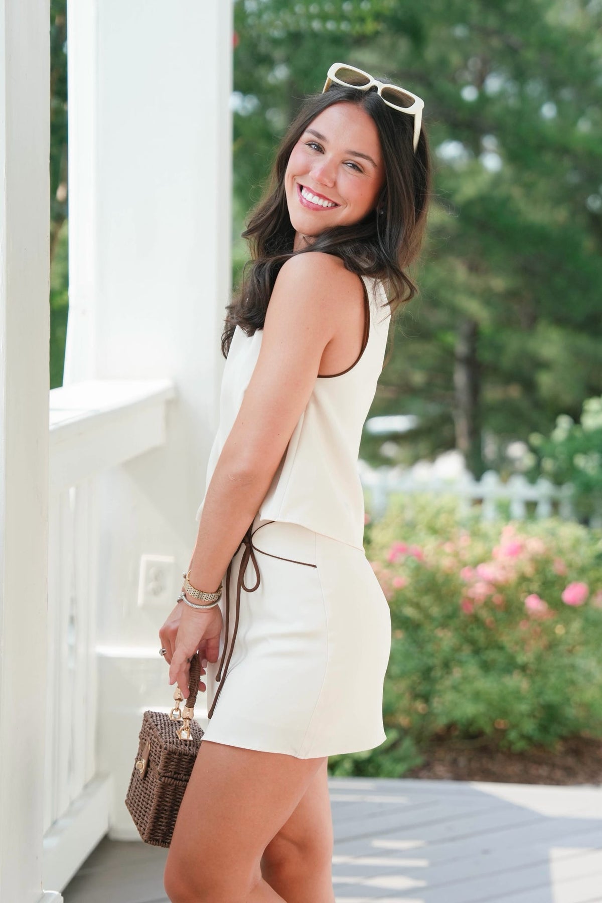 Woman in a white outfit standing outdoors with greenery in the background