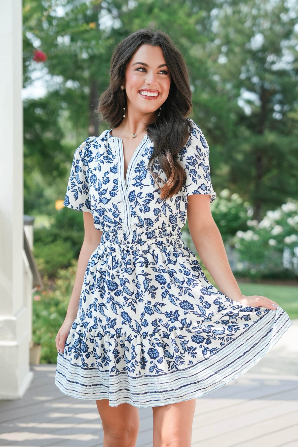 Woman wearing a blue floral dress standing outdoors with greenery in the background