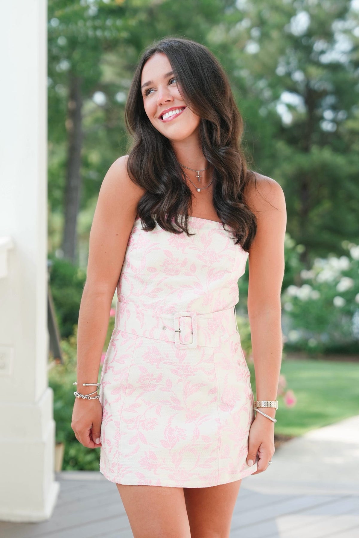 Woman in a pink dress standing outdoors with trees in the background