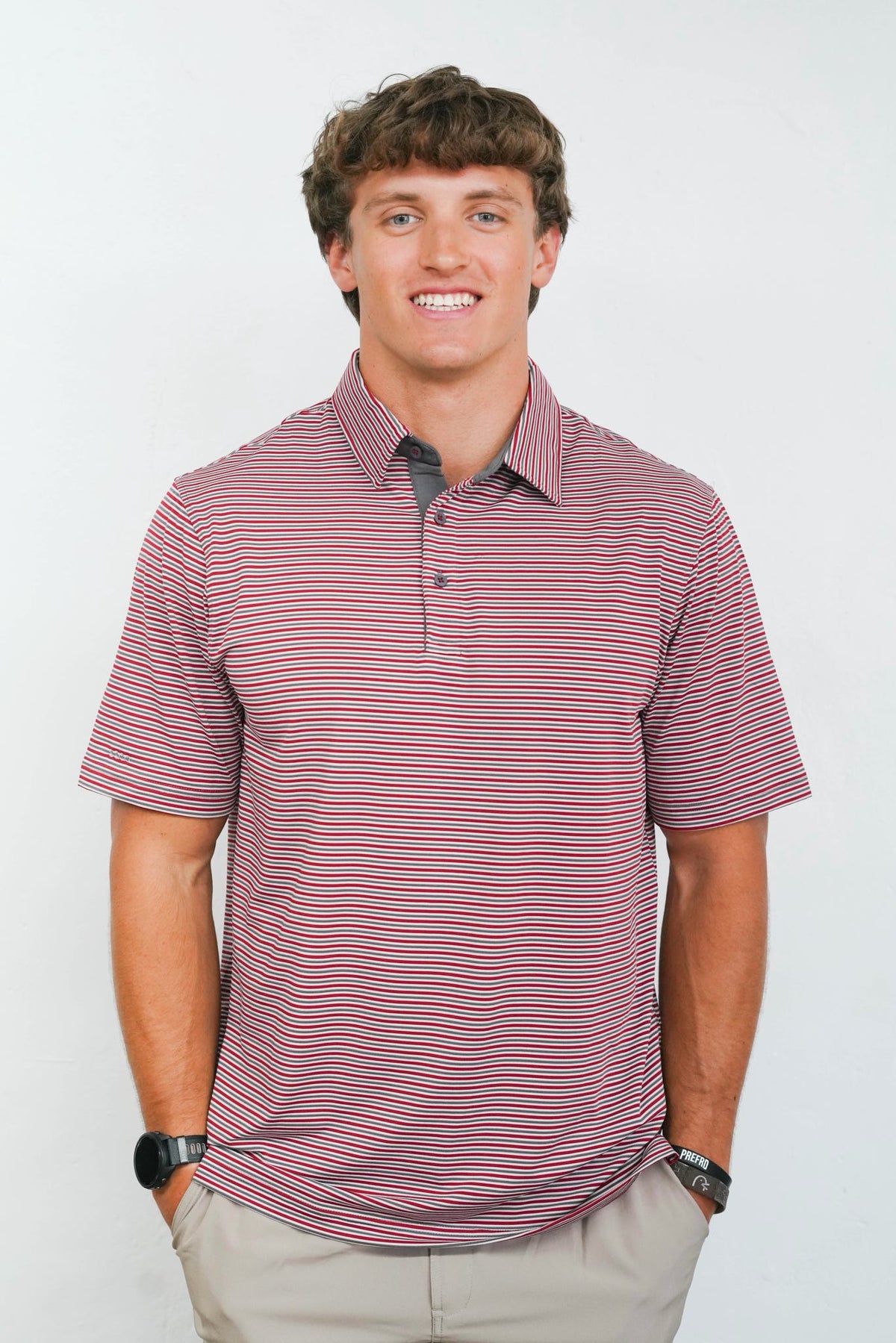 A man wearing a short-sleeve polo shirt with thin horizontal red and navy stripes on a white background.
