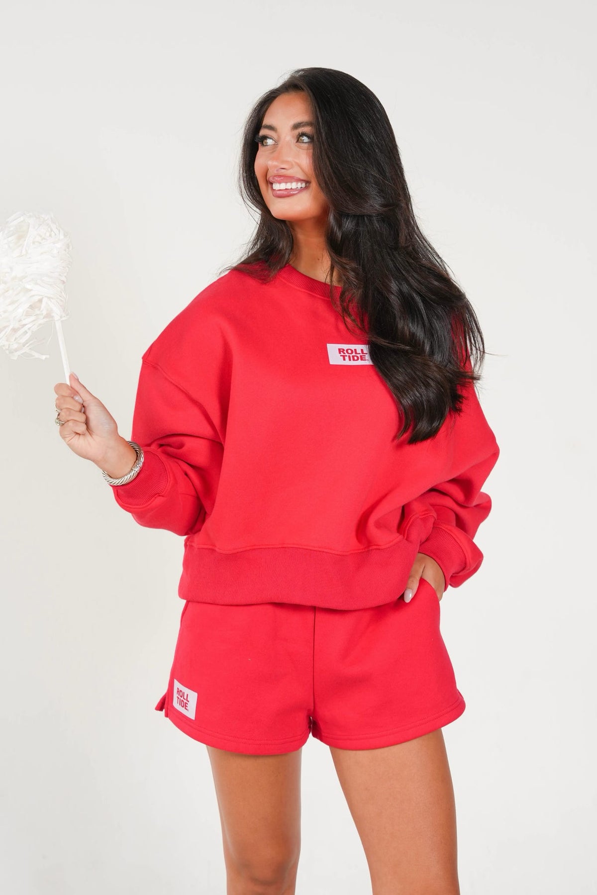 A woman modeling a matching red sweatshirt and shorts set against a plain light background, holding a white decorative fan.