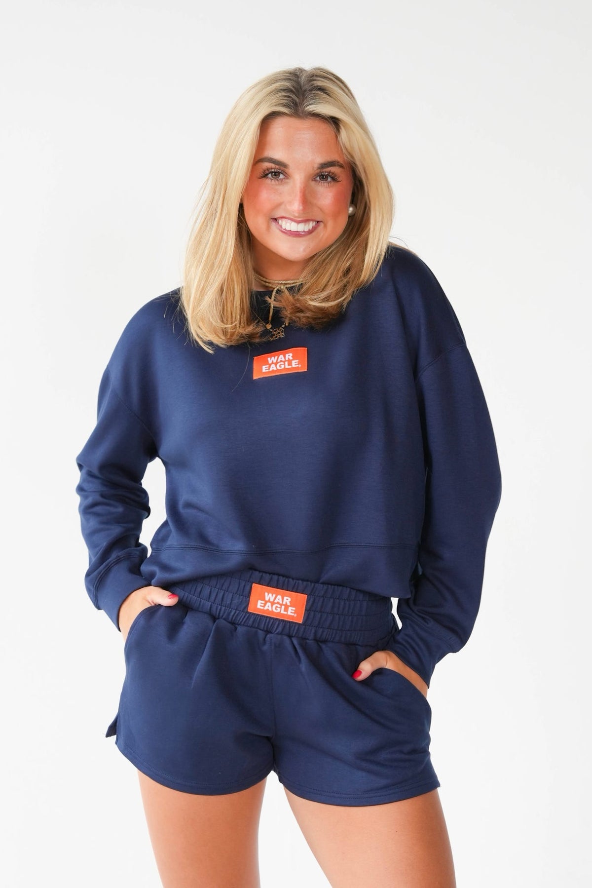 A woman modeling a navy blue sweatshirt and matching shorts set with orange 'Wear Red' logo patches, photographed against a clean white studio background.