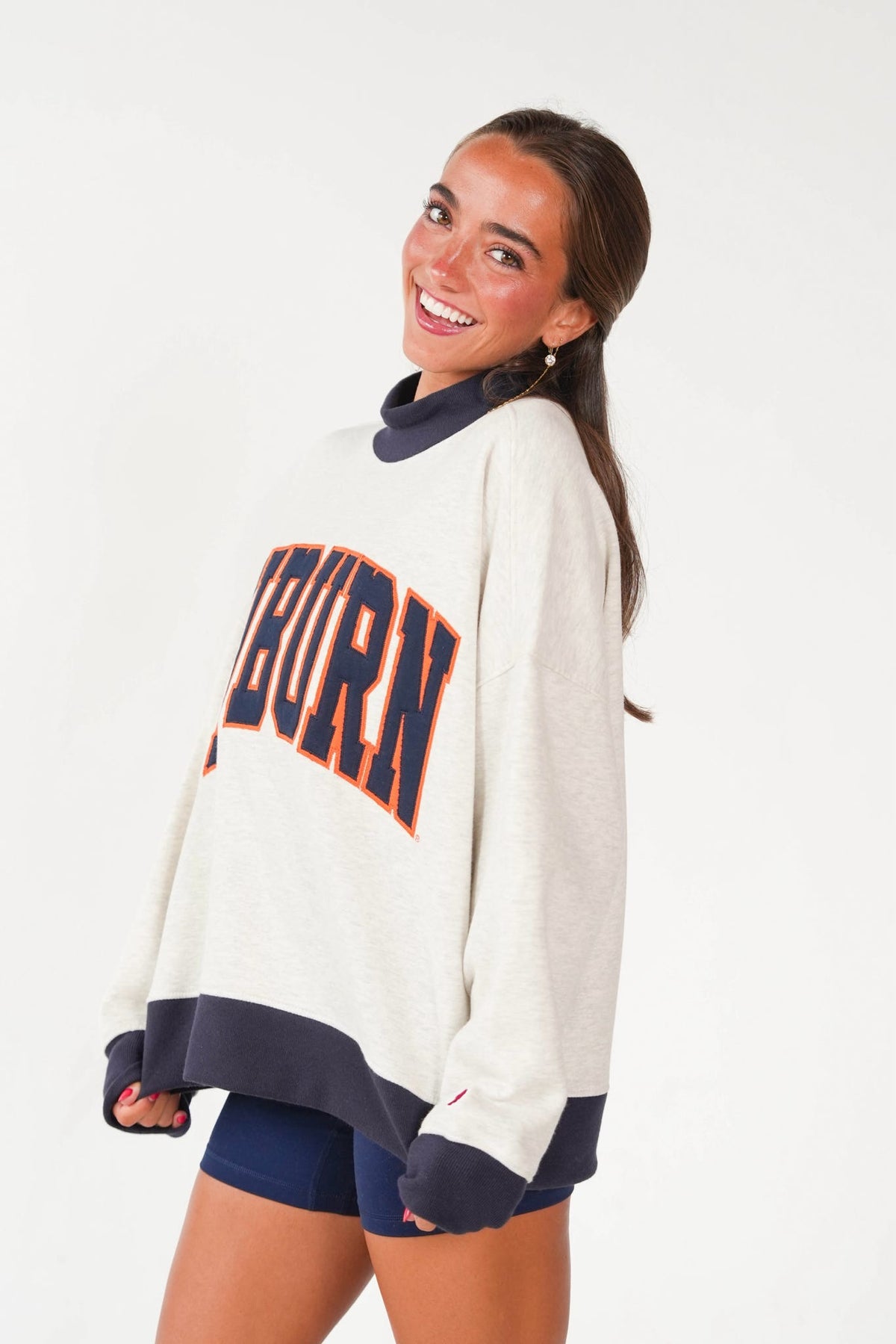 A woman wearing an oversized cream sweatshirt with navy and orange 'AUBURN' lettering, paired with navy shorts, against a plain white background.