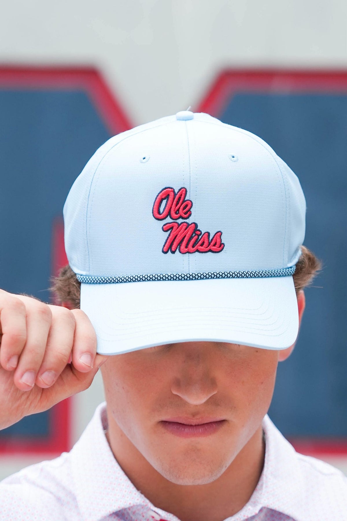 A close-up of a person wearing a white baseball cap with 'Ole Miss' embroidered in red script across the front, with a blurred outdoor background.