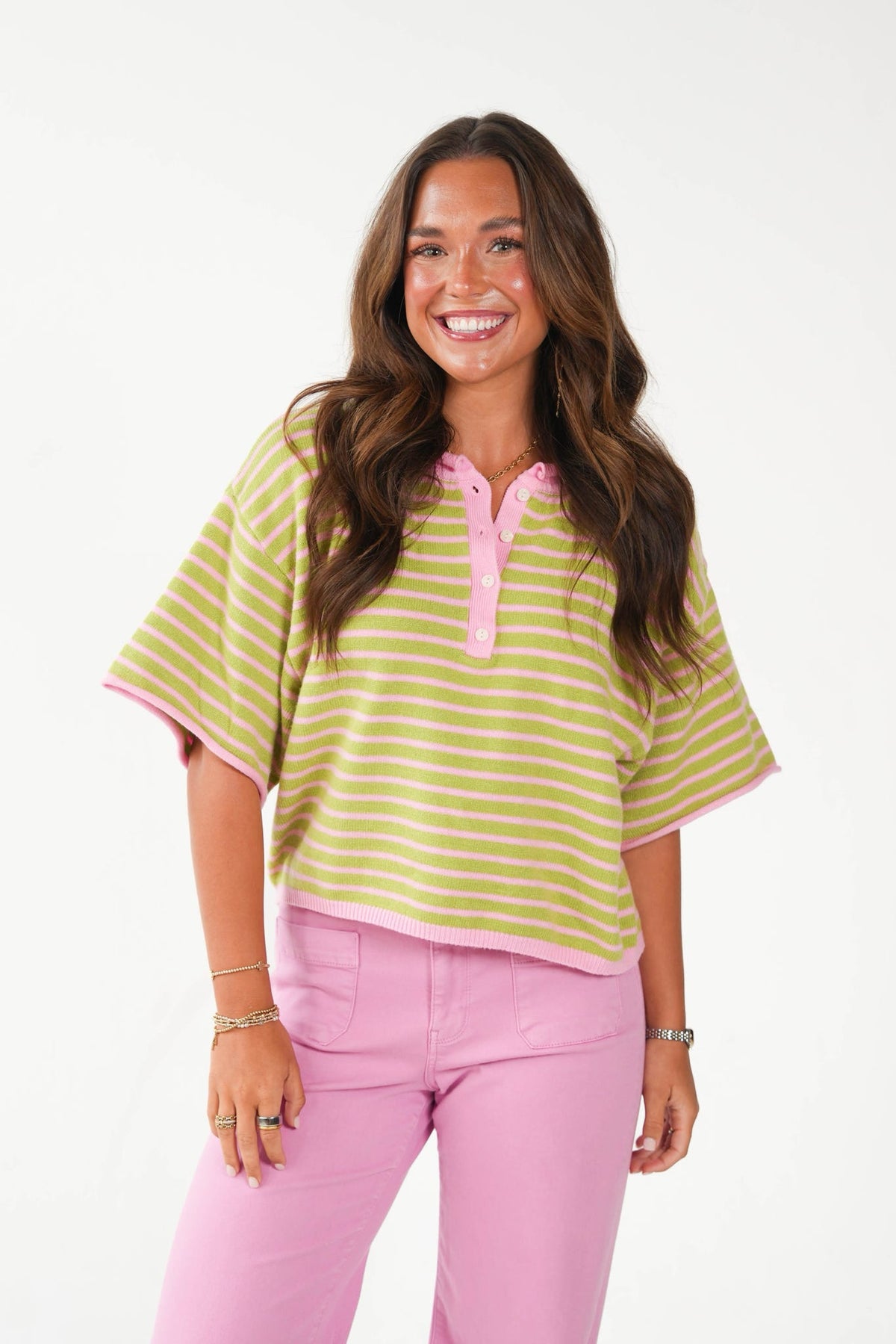 A woman modeling a short-sleeve striped top with pink trim and pink pants, standing against a plain white studio background.