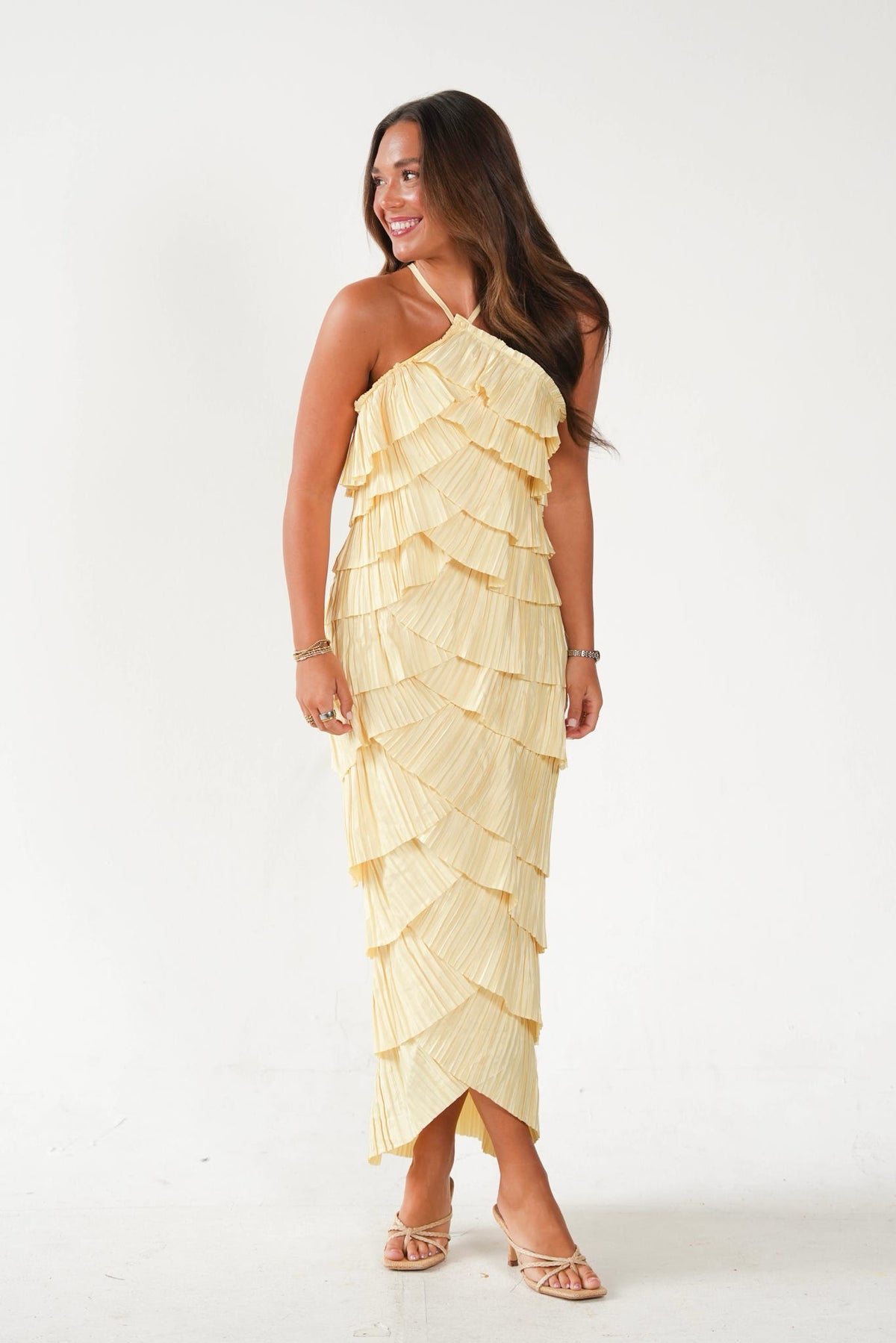A woman modeling a pale yellow ruffled halter-neck maxi dress against a plain white studio background.