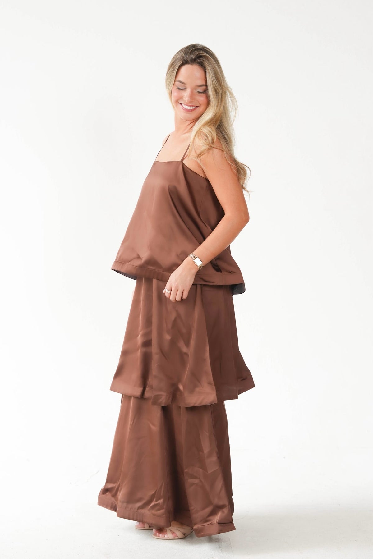A woman modeling a matching brown two-piece lounge set consisting of a sleeveless camisole top and wide-leg pants, photographed against a seamless white studio background.