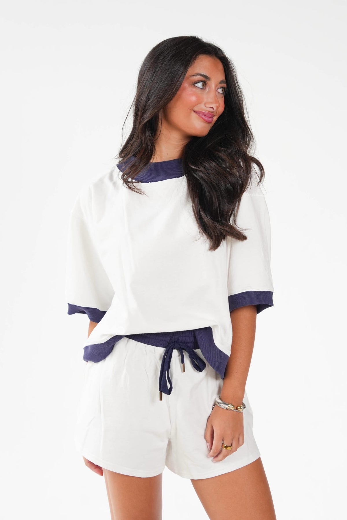 A woman modeling a white short-sleeve top and matching shorts set with dark navy blue trim, shown against a plain white studio background.
