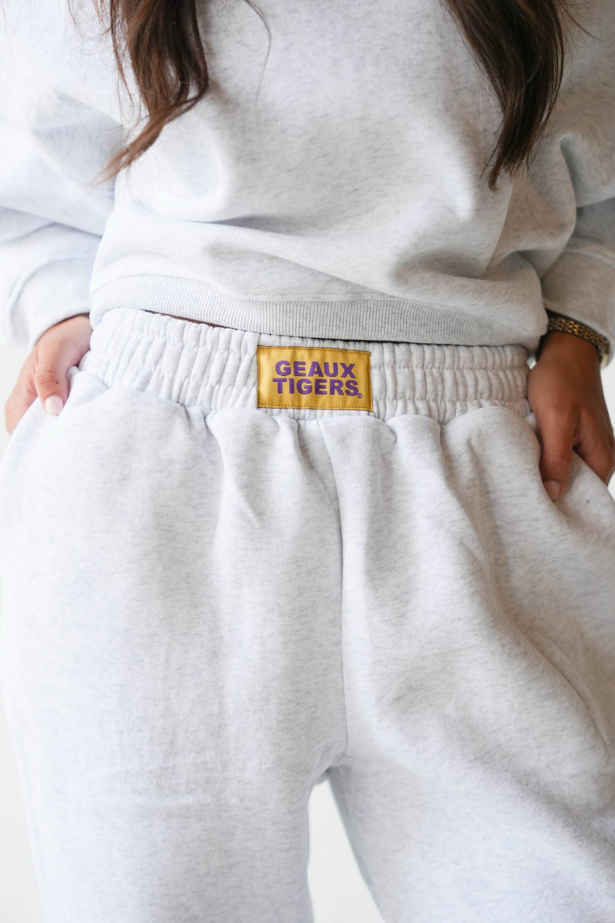 Close-up of a person wearing light heather gray sweatpants with a yellow waistband patch reading 'GEAUX TIGERS' and a matching light gray sweatshirt.