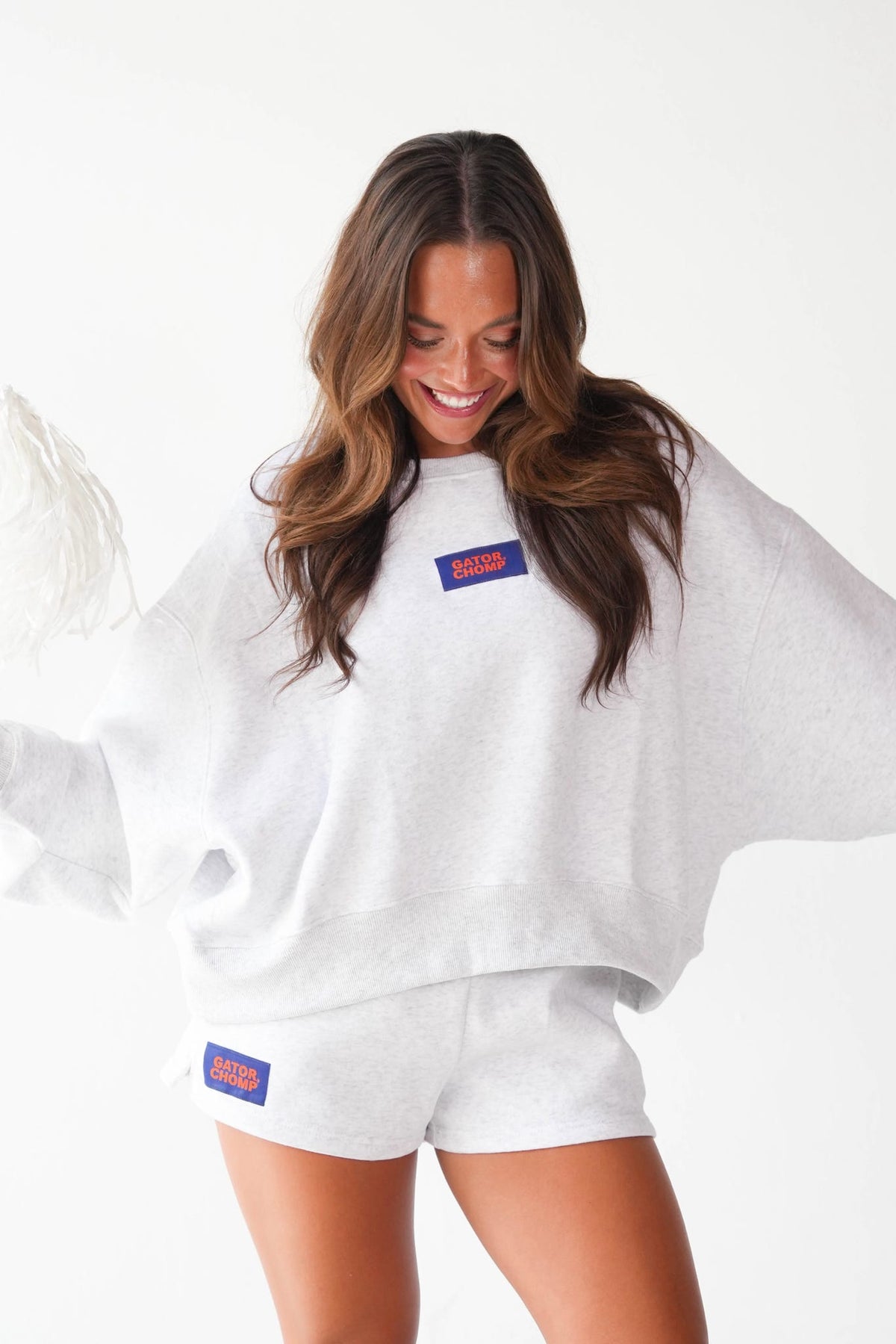 A woman wearing a white oversized sweatshirt and matching shorts with blue and red 'BAGS' patches on the chest and hip, posed against a clean white background.