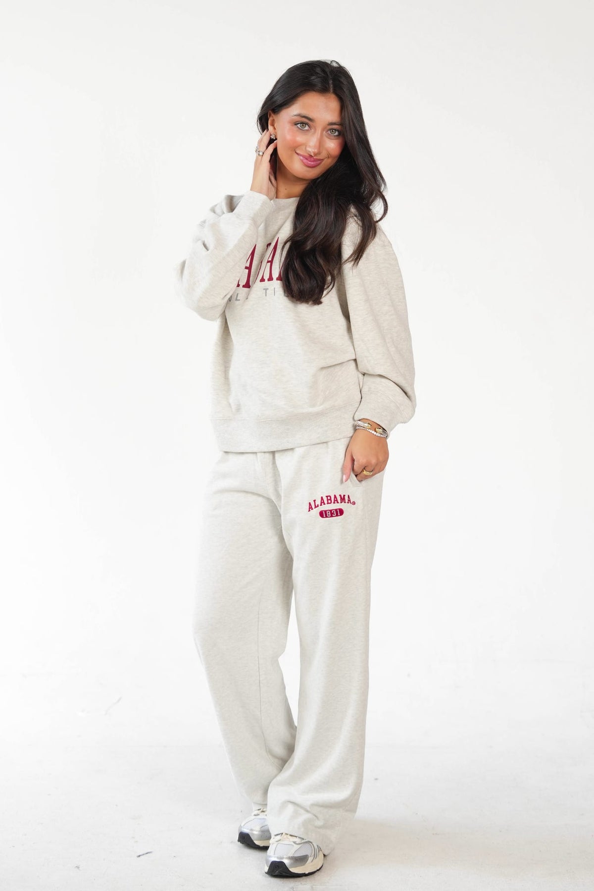A woman modeling a matching light beige sweatshirt and sweatpants lounge set with red collegiate lettering that reads 'ALABAMA GAMEDAKS' on a plain white studio background.