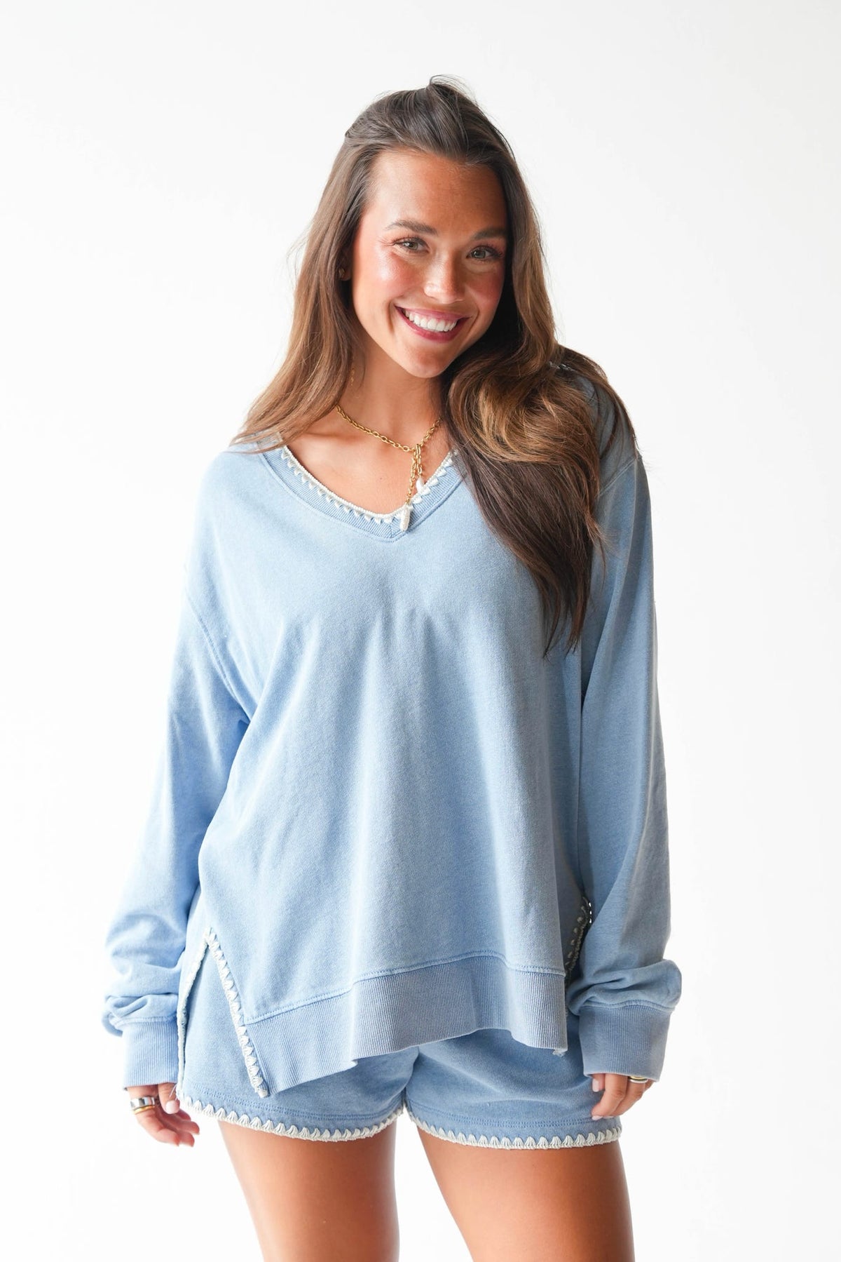 A woman modeling a light blue lounge set consisting of a long-sleeve V-neck top and matching shorts with white crochet trim, set against a plain white background.