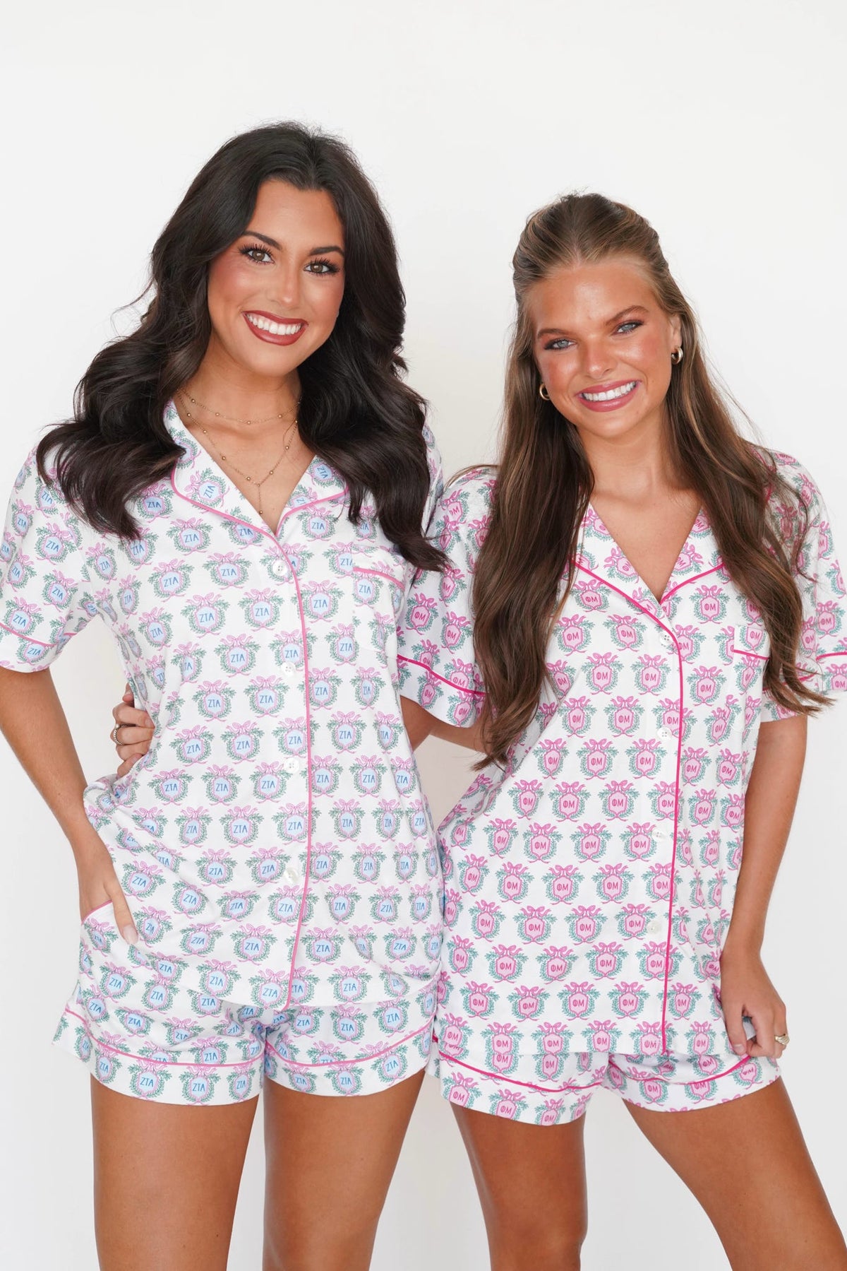 Two women modeling matching short-sleeve pajama sets with a white base and a pink and blue teddy bear pattern, standing against a plain white background.