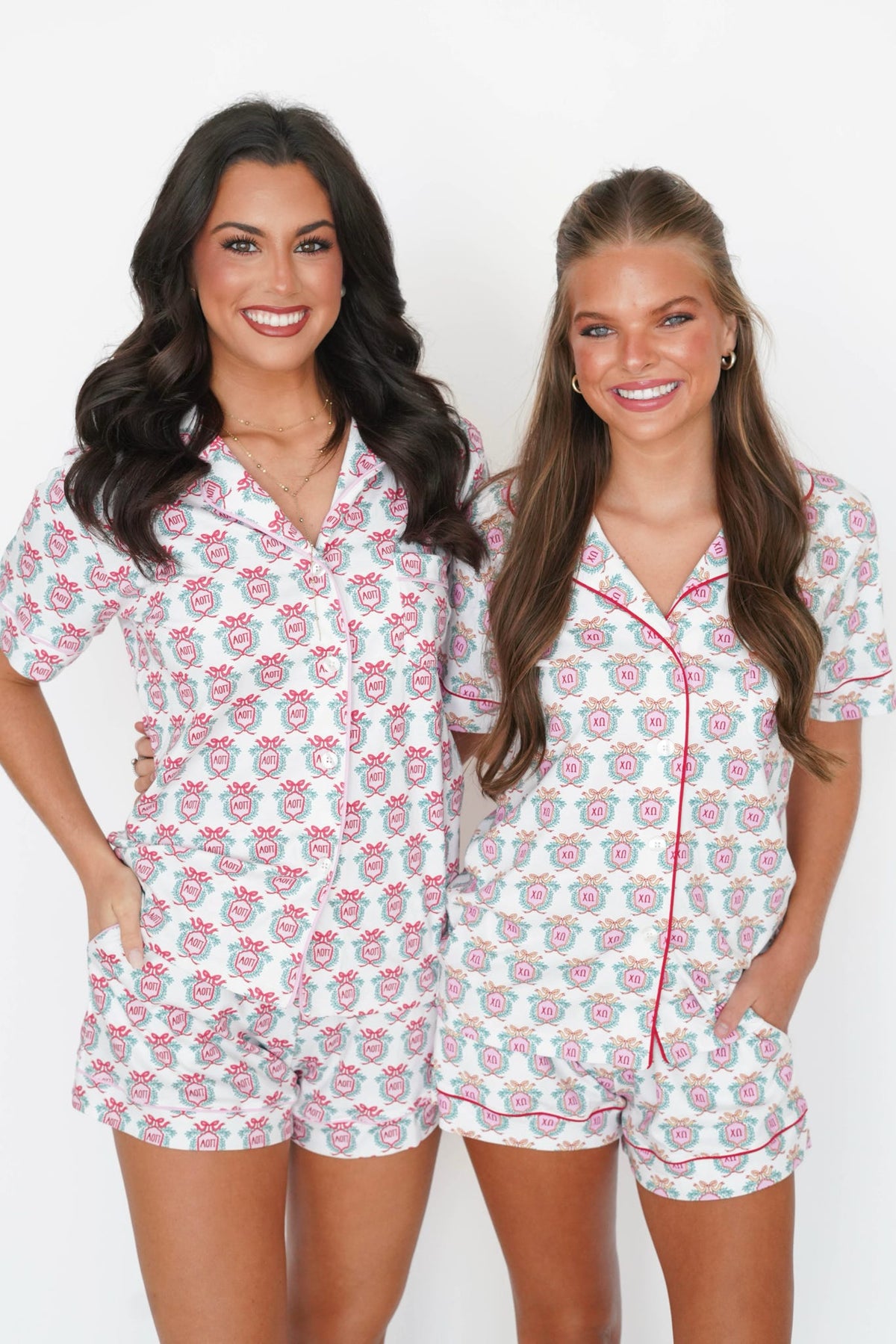 Two women modeling matching white short-sleeve pajama sets with a pink and gray floral pattern and red piping, standing against a plain white background.
